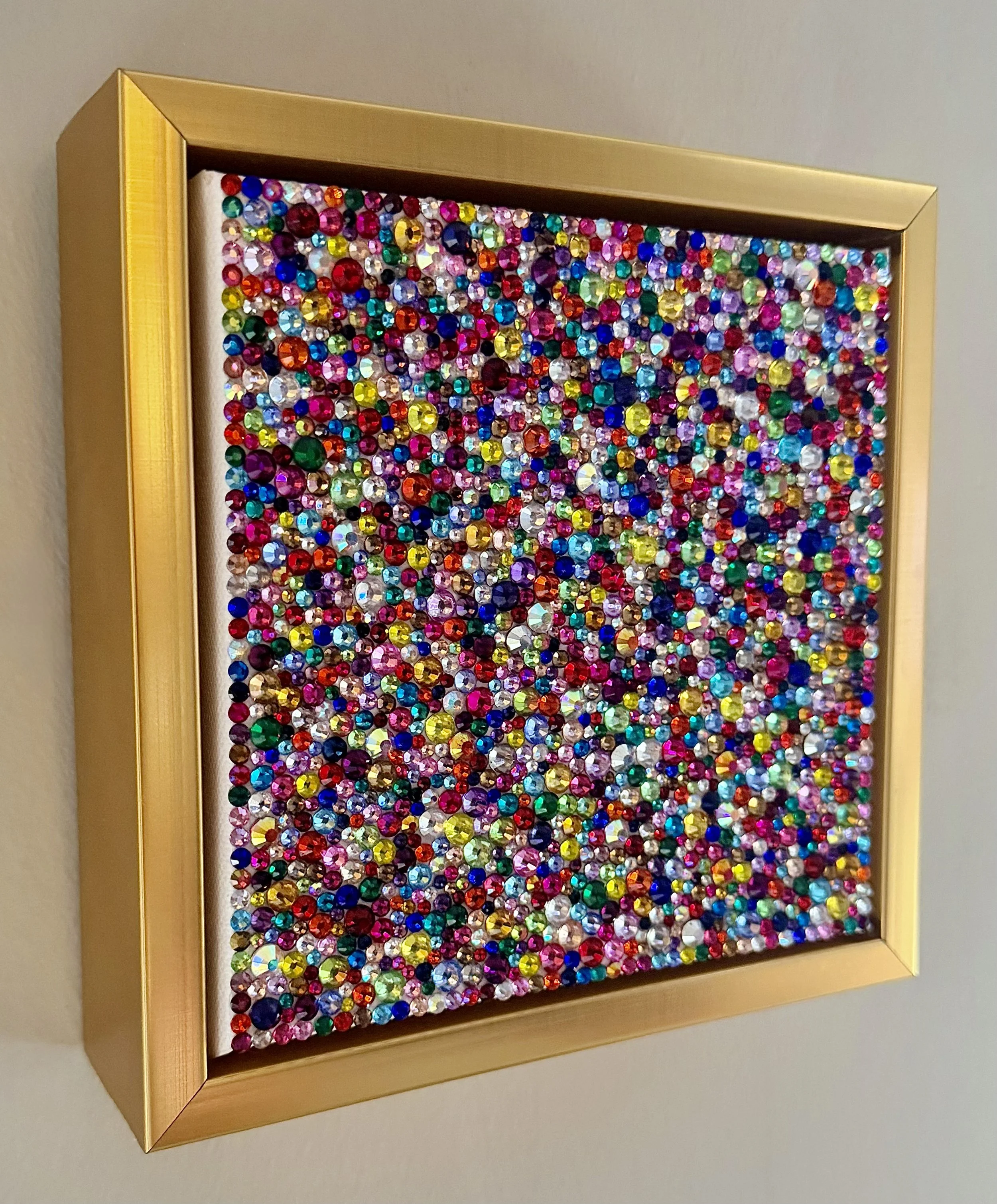 Angled side-view of "Frenzy," showing the textured depth of multi-colored rhinestones within a gold floating frame.