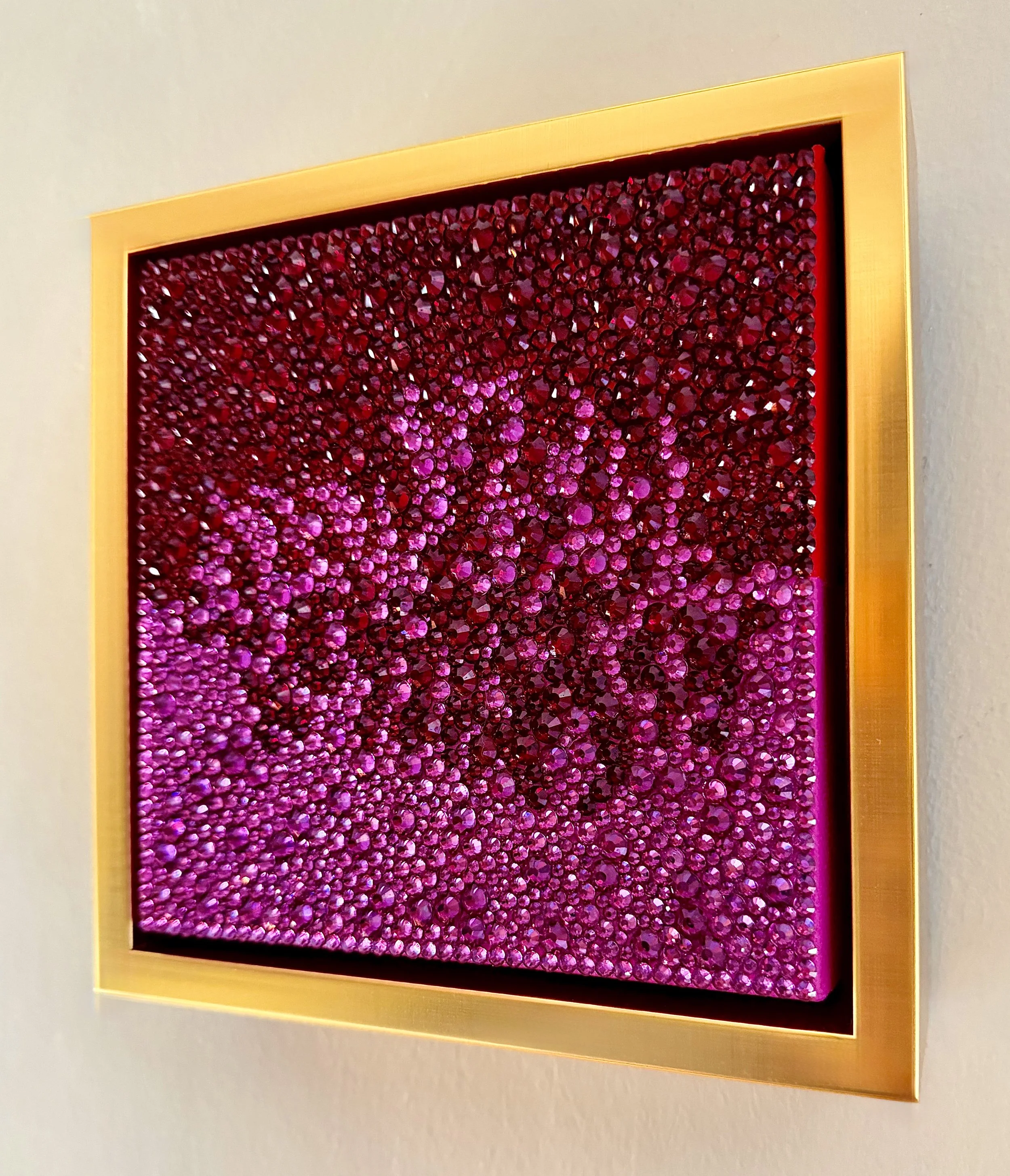 Profile of a 6x6-inch sculptural artwork titled "Ardor" featuring a dense, high-relief field of fuchsia and crimson rhinestones set within a gold floating frame.