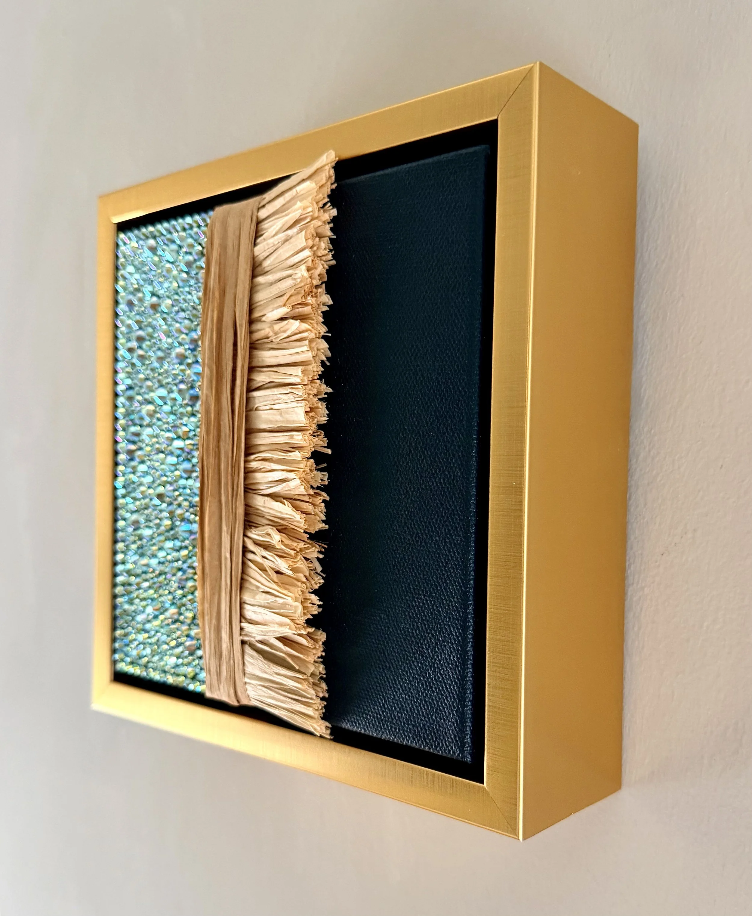 A profile image of "Futile" a 6x6 inch mixed-media piece of teal rhinestones and natural raffia in a brushed-gold floating frame.
