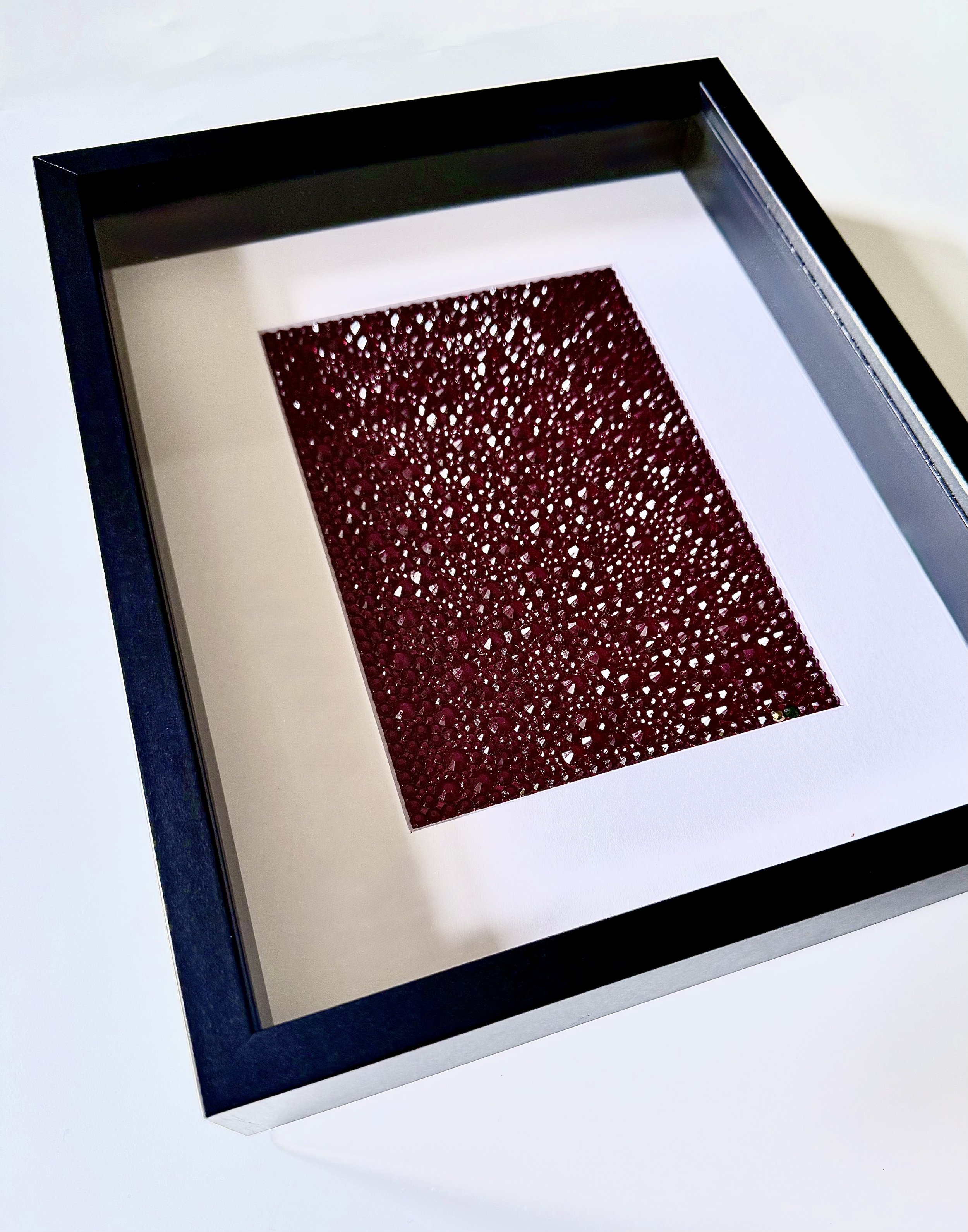 Angled view of framed crimson rhinestone art piece titled "Convergence."