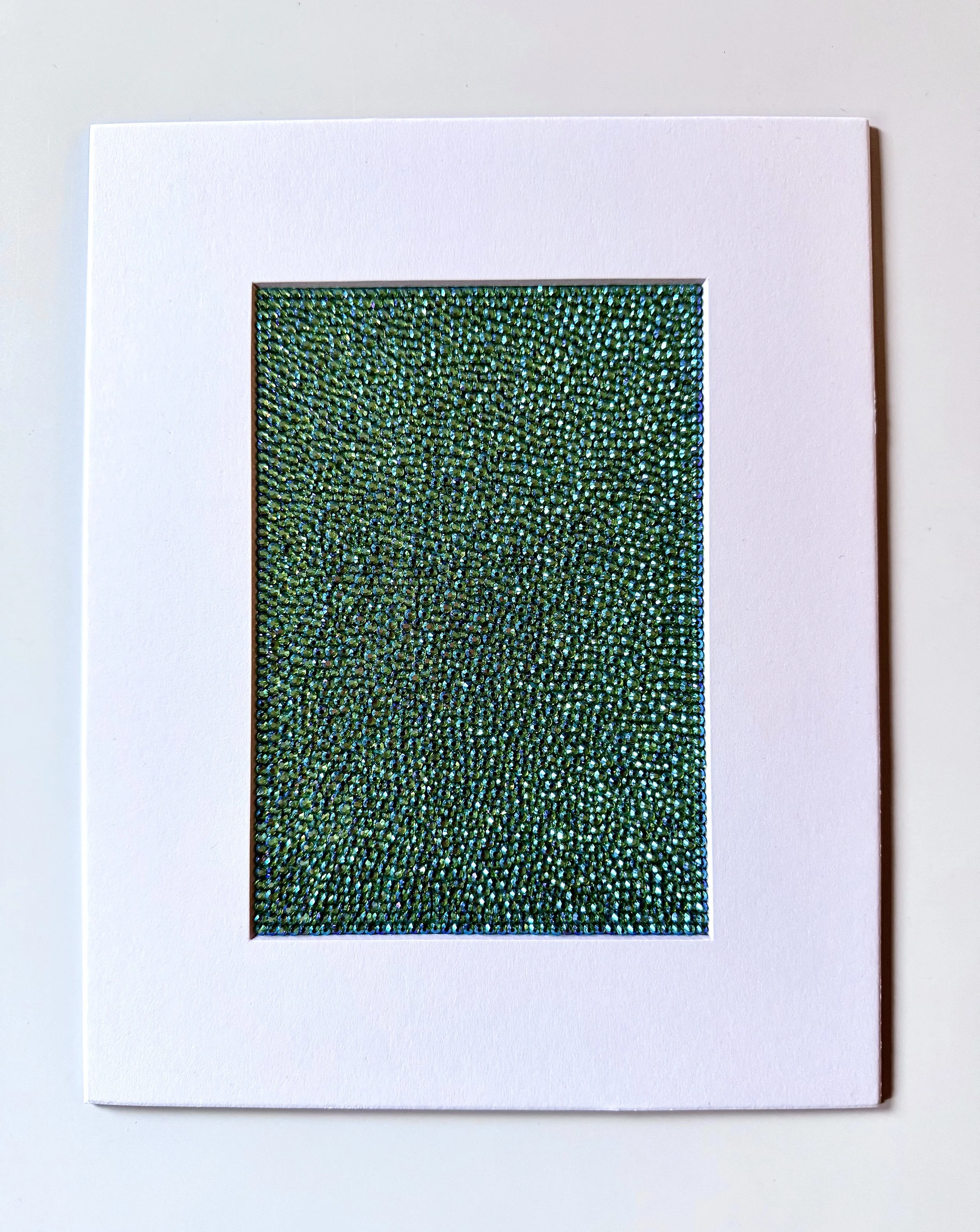 Hollow, 2026. 5 x 7 in. [matted to 8 x 10 in.] A dense, shimmering field of peridot ab glass rhinestones on watercolor paper, presented within a clean white mat.