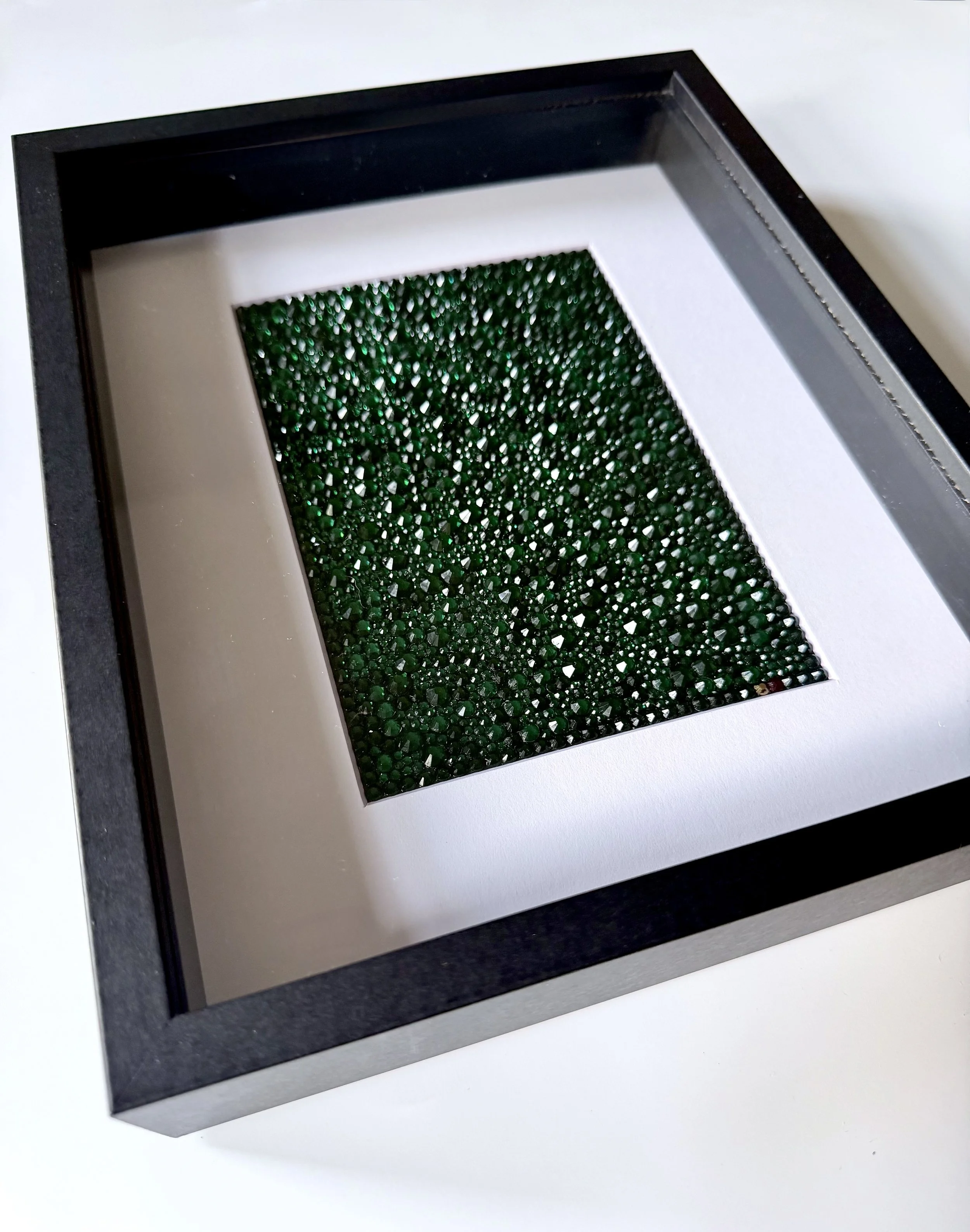 Angled view of framed emerald rhinestone art piece titled "Continuum."