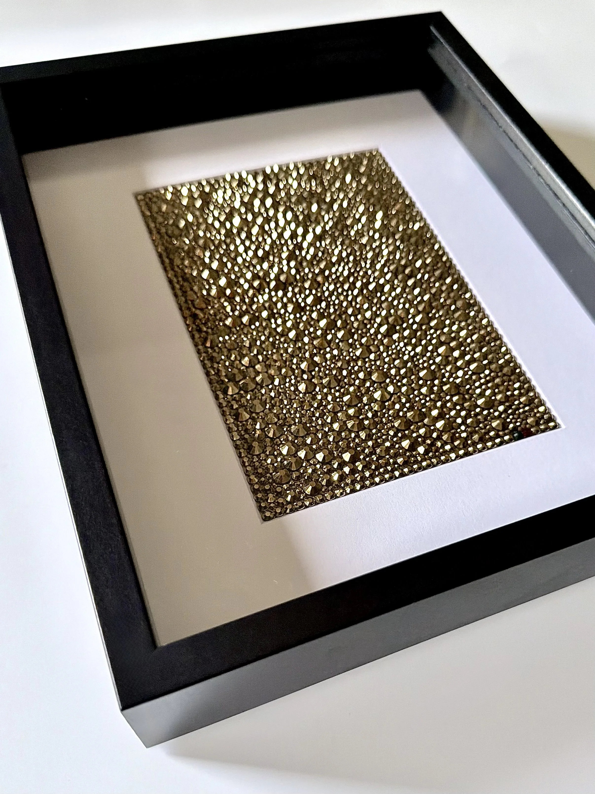 Angled view of framed gold rhinestone art piece titled "Resonance."
