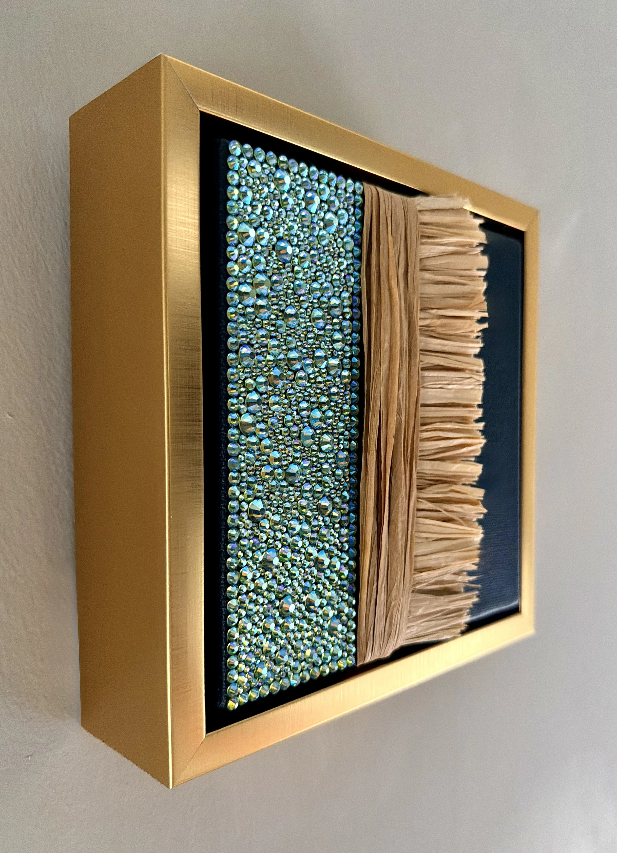 A profile image of "Futile" a 6x6 inch mixed-media piece of teal rhinestones and natural raffia in a brushed-gold floating frame.