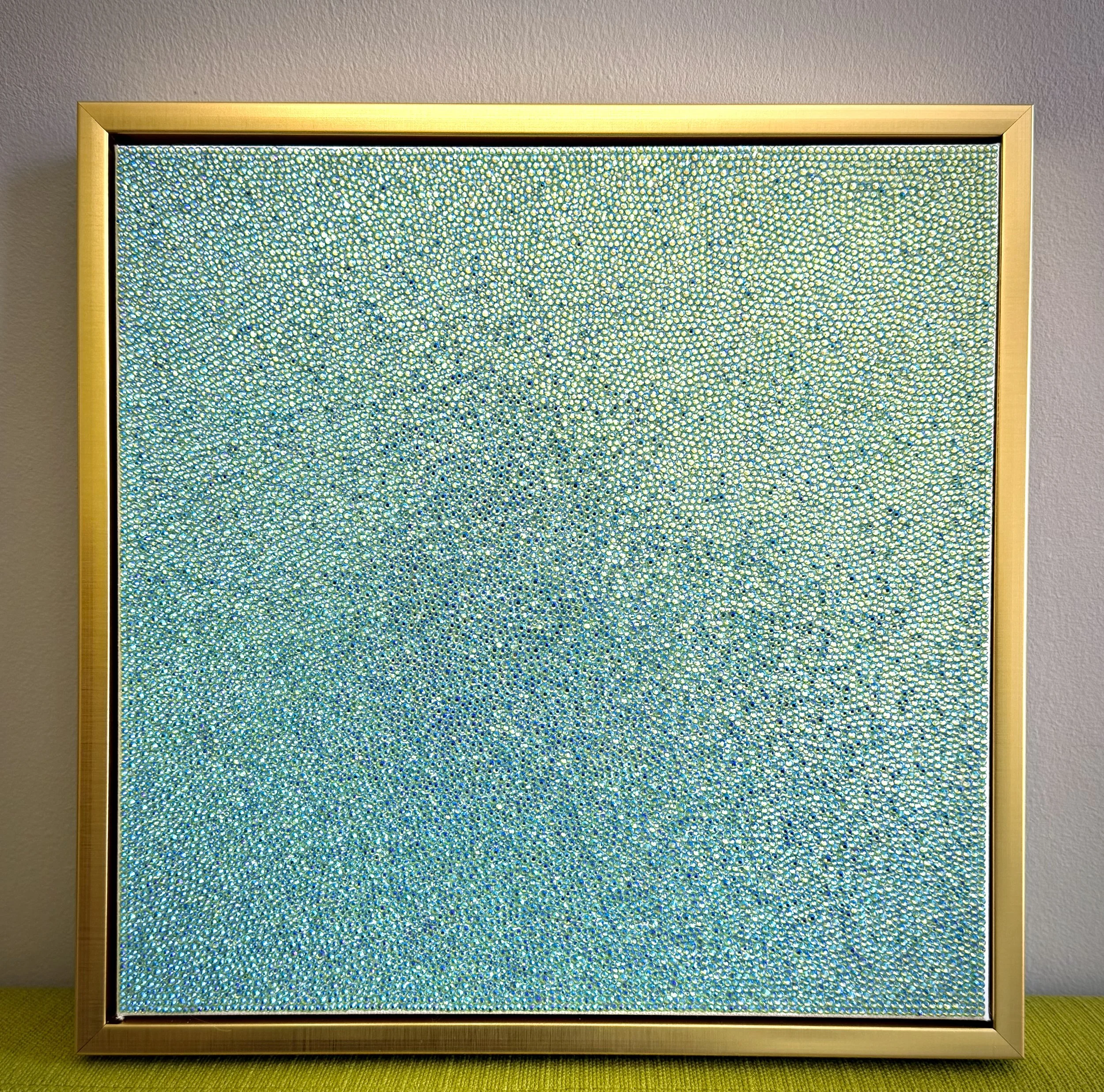 Devoid (2025) displayed on a green couch. The 12x12 in. peridot panel’s prismatic shimmer contrasts with the bright green upholstery.