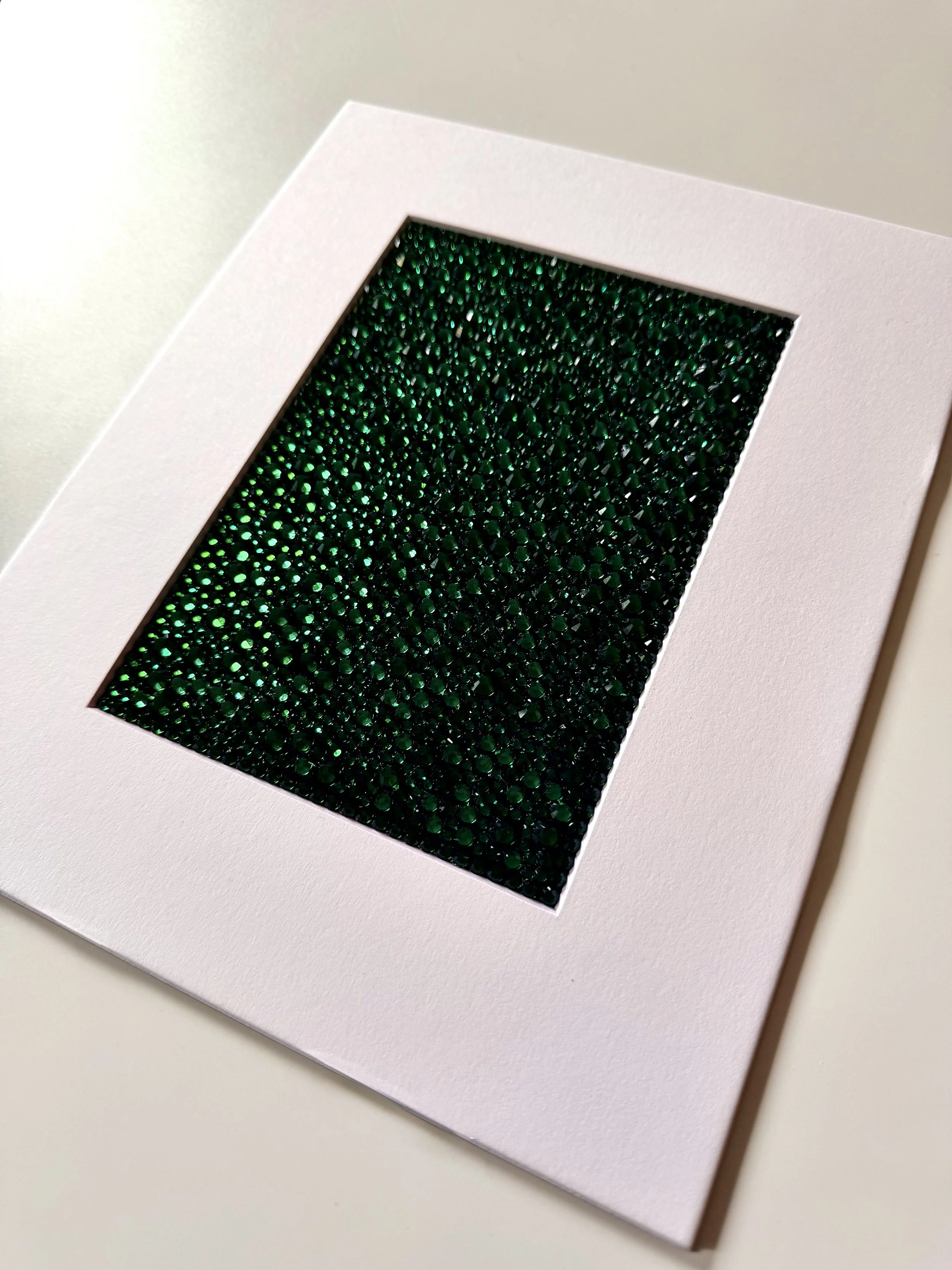 An angled close-up of the "Covet" paper study, showing the high-relief texture of the emerald green rhinestone field.
