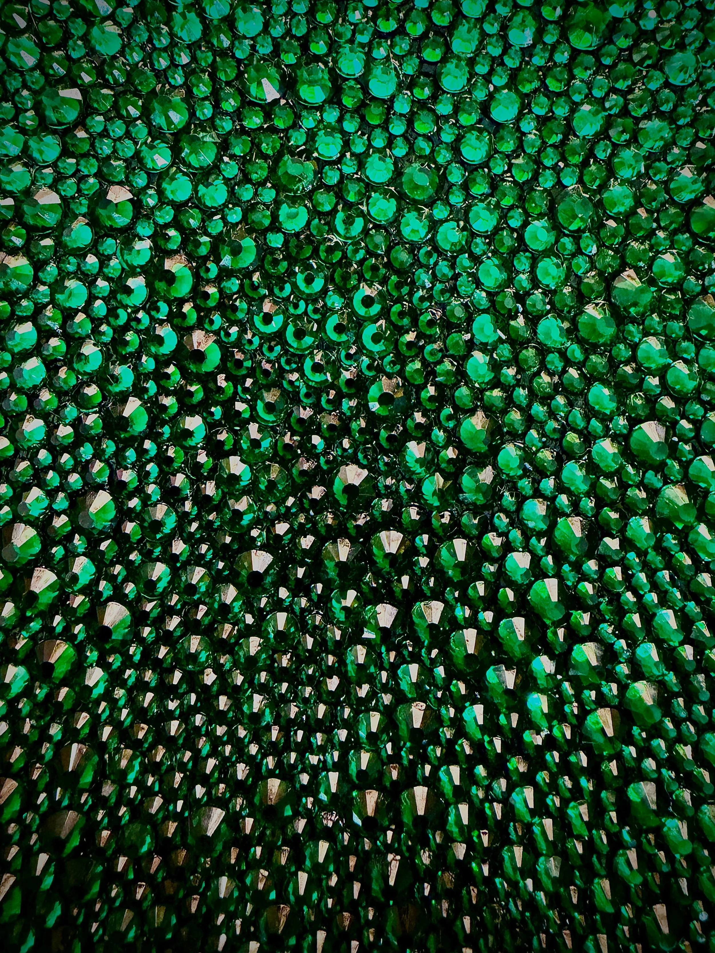 Macro detail of Greed (2026). Close-up of faceted emerald glass rhinestones, showing the light-catching texture and dense, rhythmic placement.