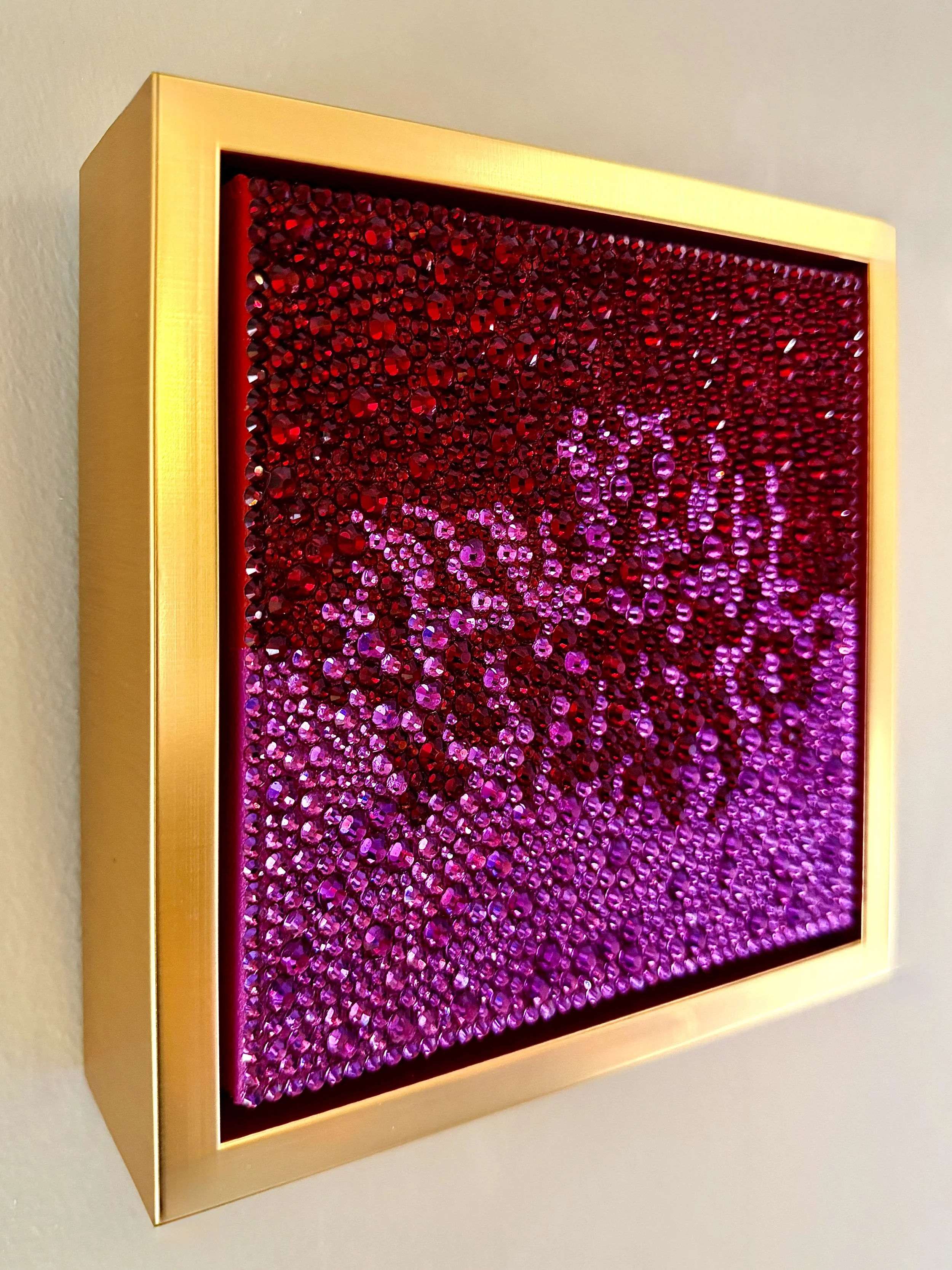 Profile of a 6x6-inch sculptural artwork titled "Ardor" featuring a dense, high-relief field of fuchsia and crimson rhinestones set within a gold floating frame.
