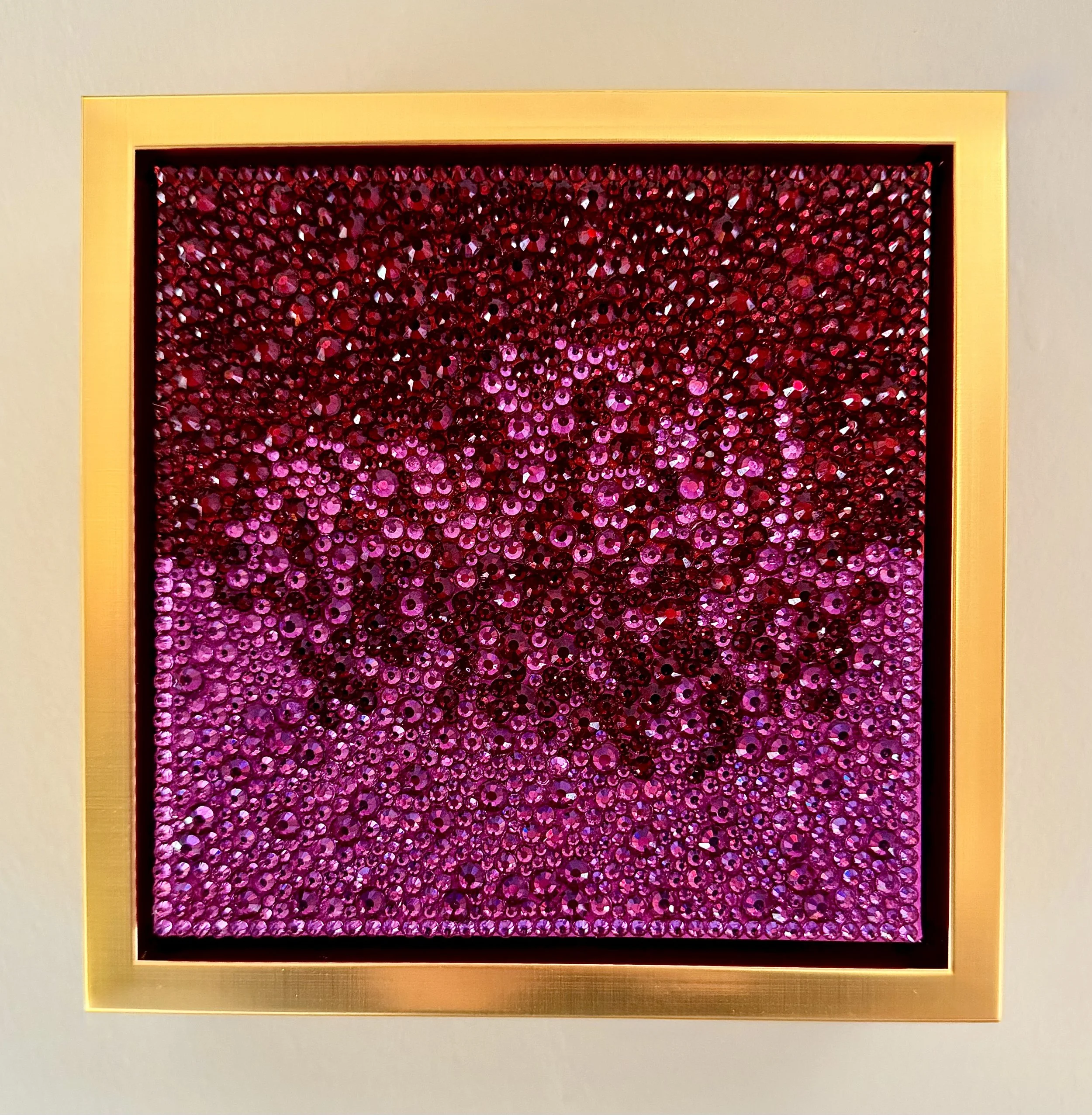 Ardor, 2026. 6 x 6 in. A monochromatic sculptural panel featuring hand-placed crimson and fuchsia glass rhinestones set within a gold floating frame.