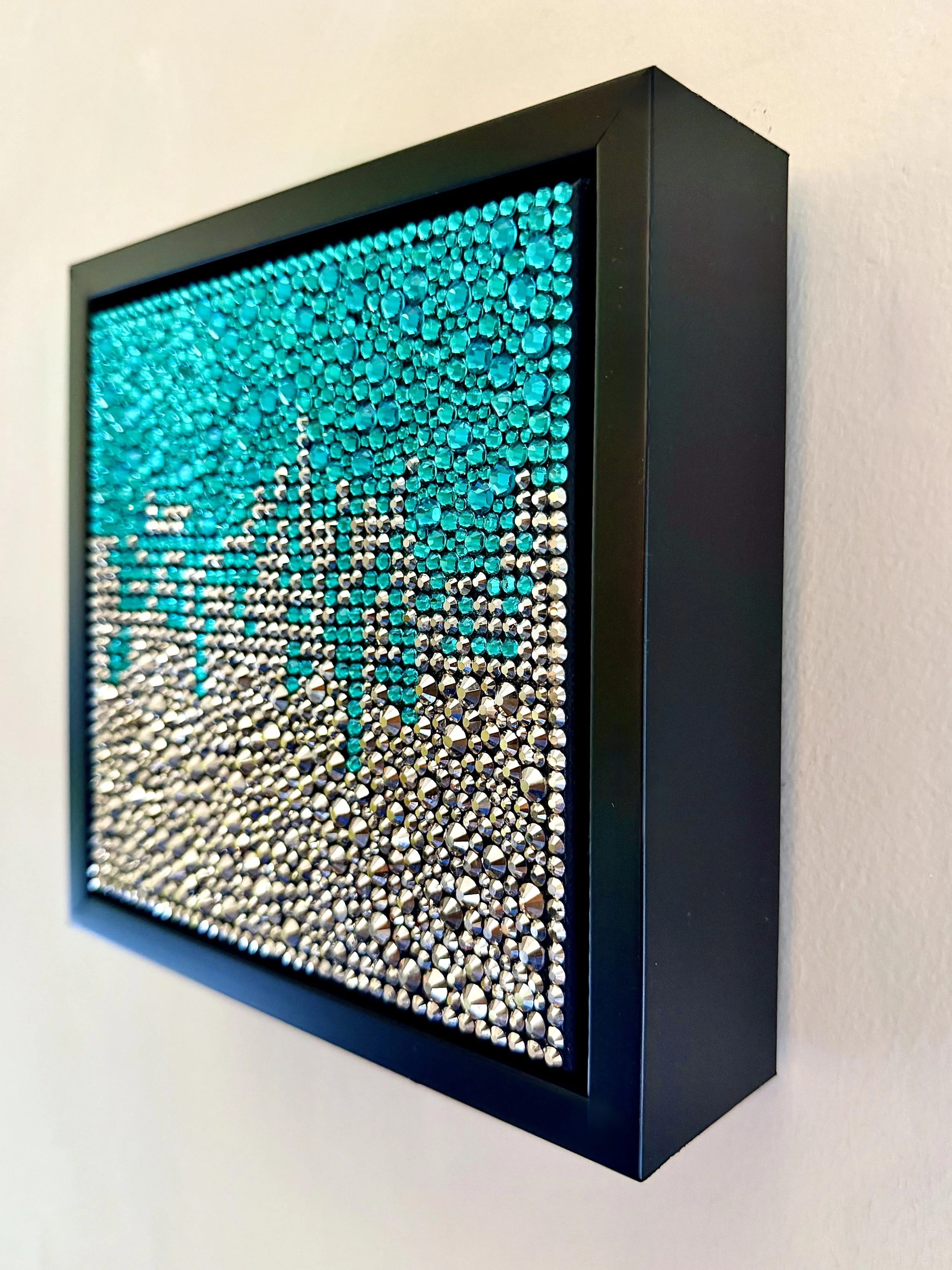 Profile of a 6x6-inch sculptural artwork titled "Bitter" featuring a high-relief field of teal and hematite rhinestones in a black floating frame.