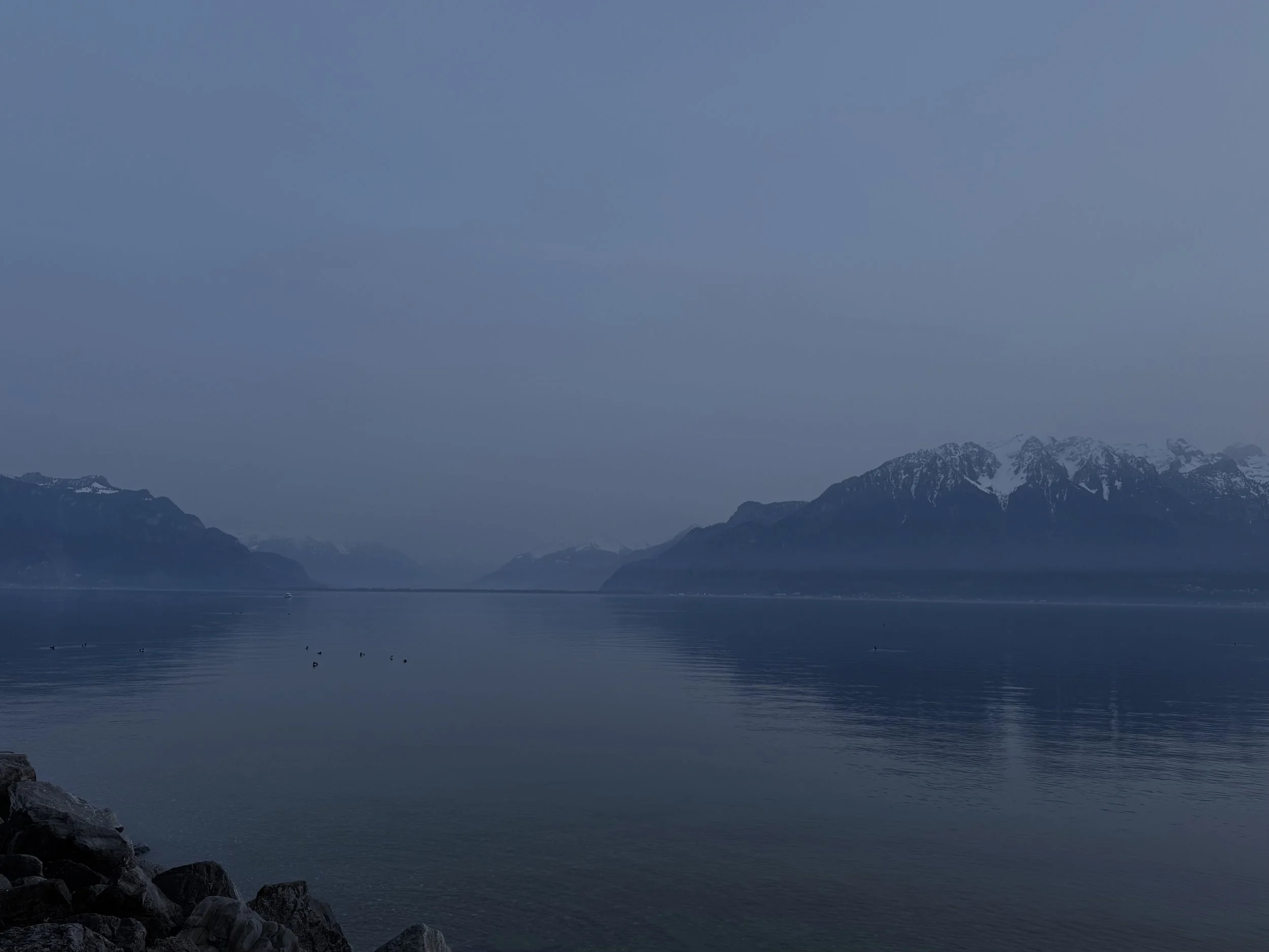 Calm lake with mountains in the background and a rocky shoreline in the foreground.