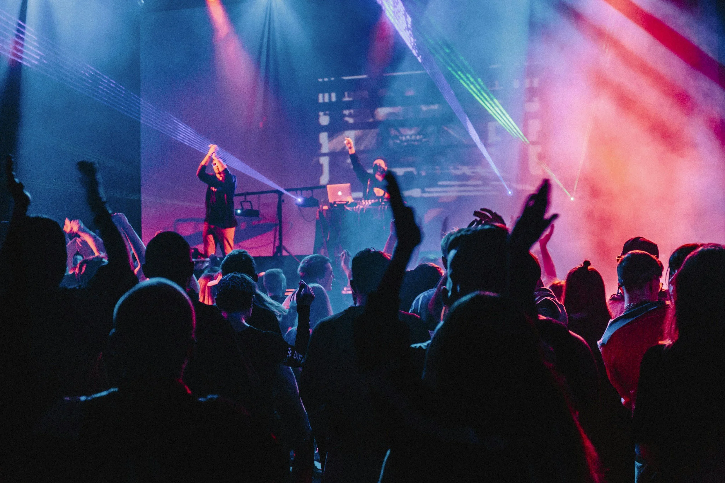 Un concierto con una audiencia disfrutando, luces de colores y un DJ en el escenario.