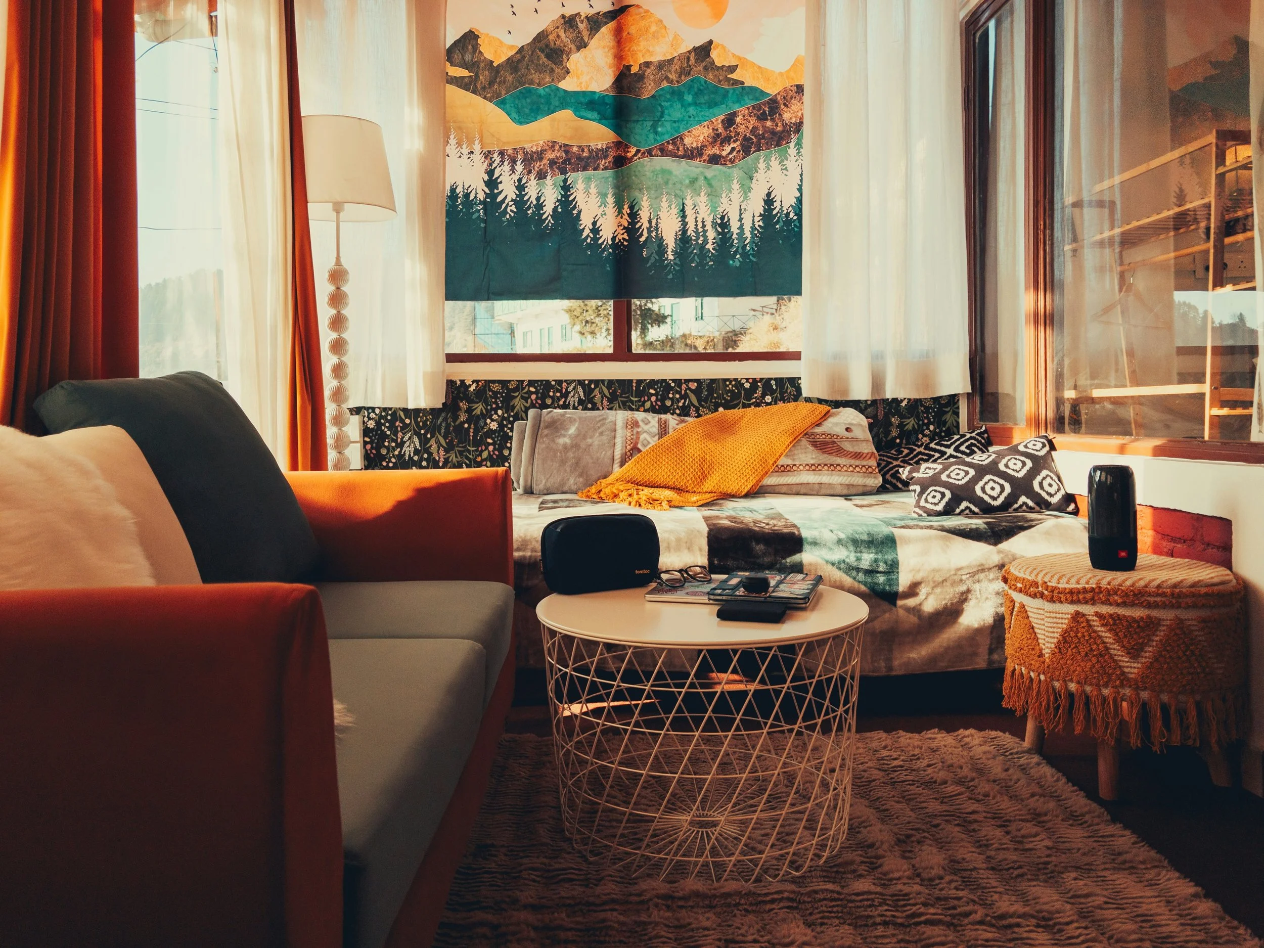 Gemütliches Wohnzimmer mit einem Sofa, Sessel, Couchtisch, Wandbild mit Berglandschaft, Vorhängen und Couchtischdecke in Erdtönen und Naturdekor.