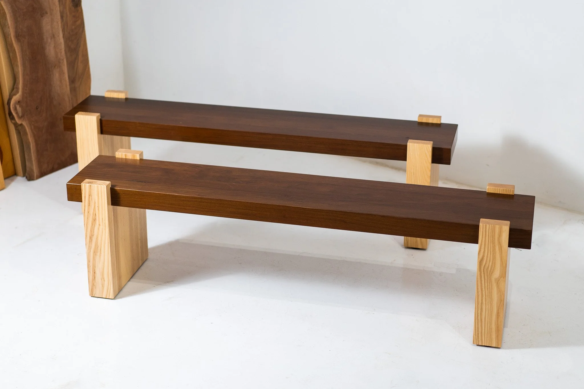 Two minimalist wooden benches made of dark and light wood, placed in a simple indoor setting.