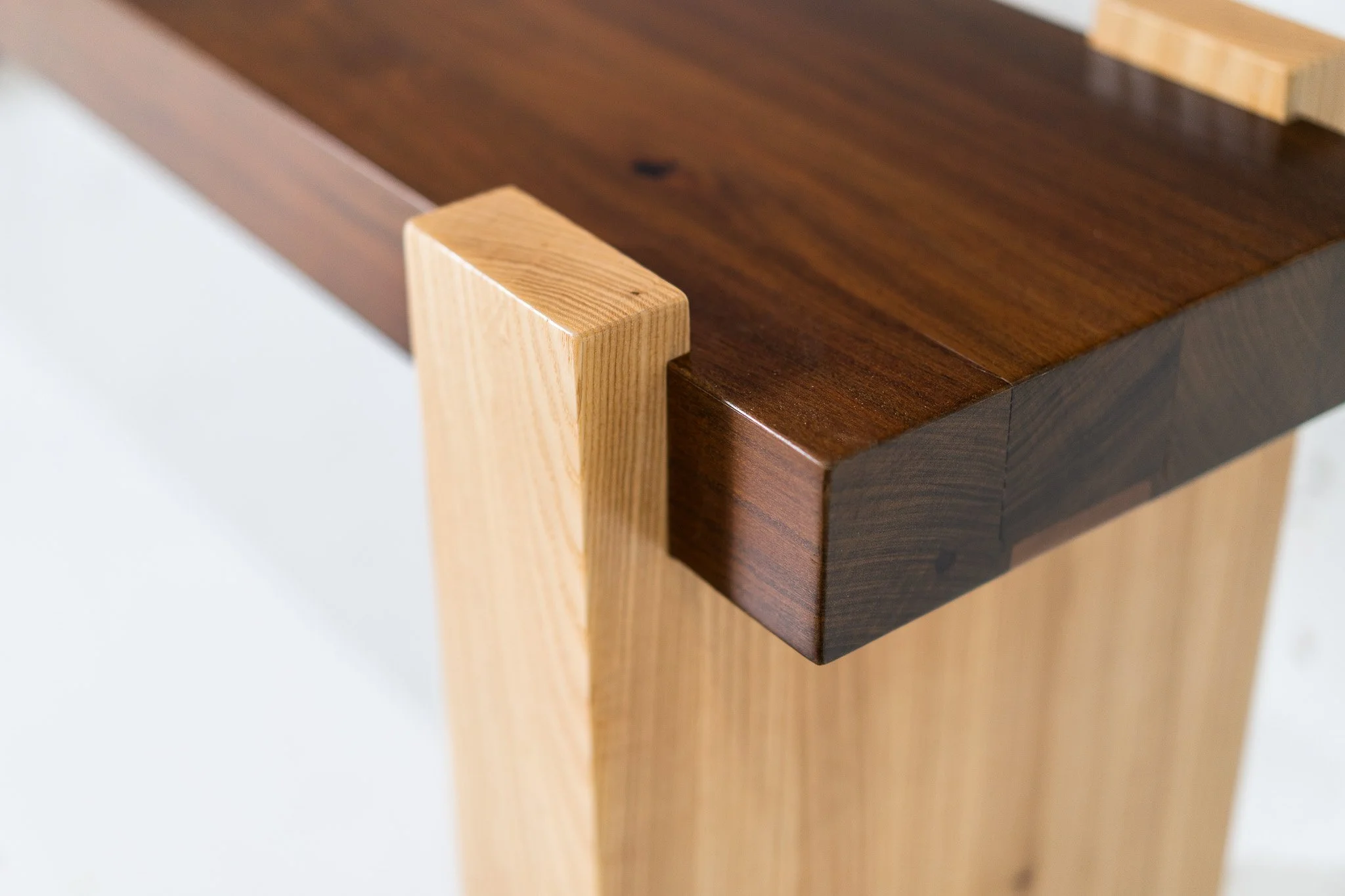 Close-up of a piece of furniture showing the corner joint of a dark wood top with a lighter wood leg.