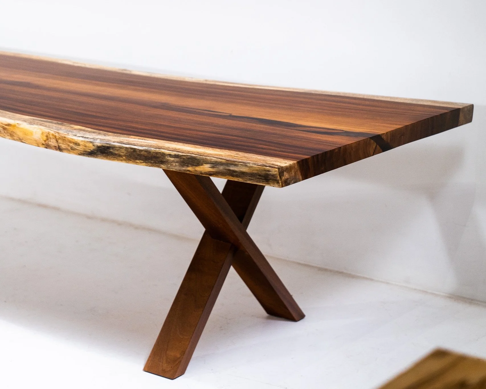 Close-up view of a wooden table with a smooth, polished surface and angled legs, set against a plain white background.