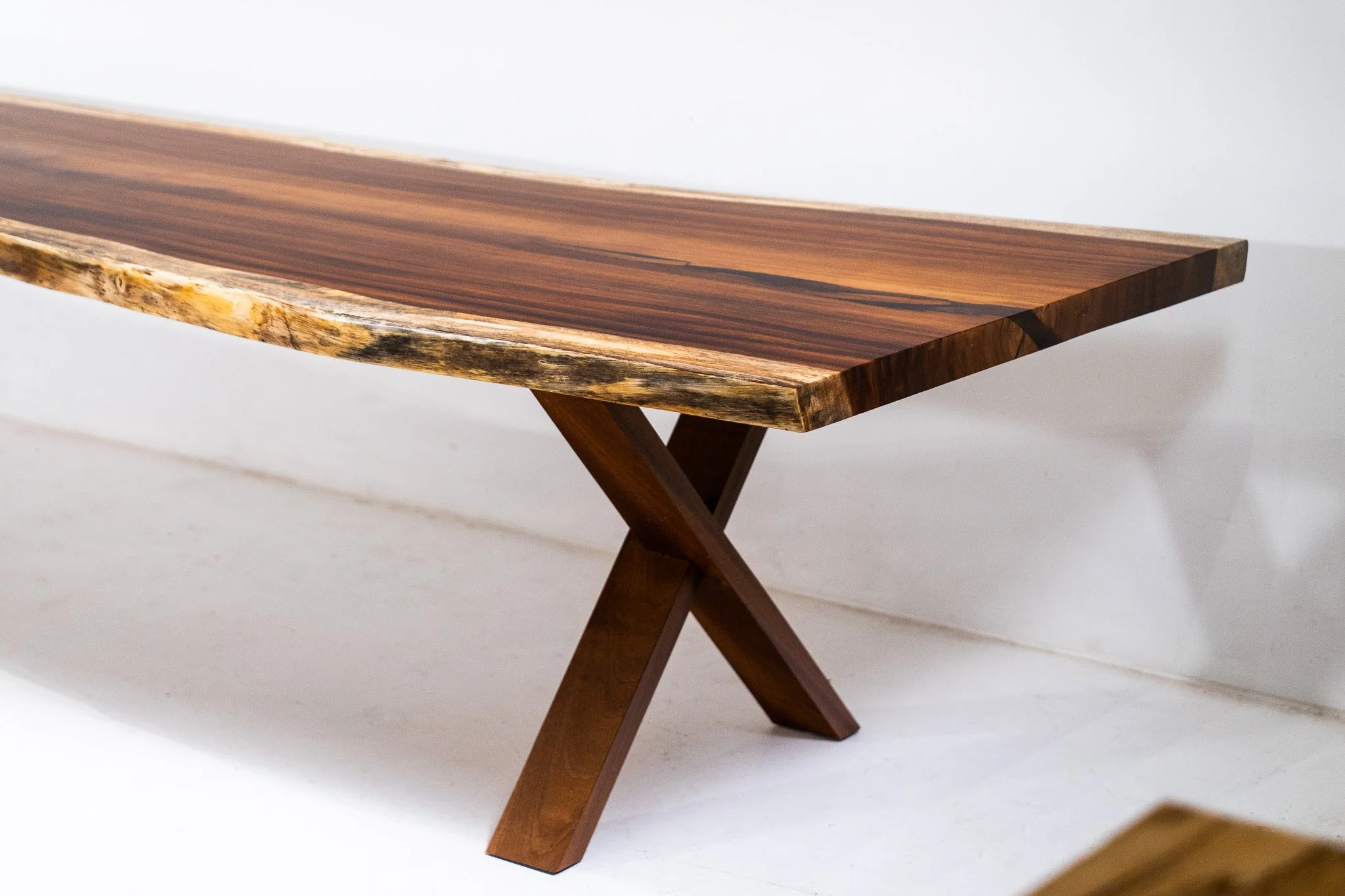A wooden table with a smooth, polished surface and a natural edge design, supported by crossed wooden legs.