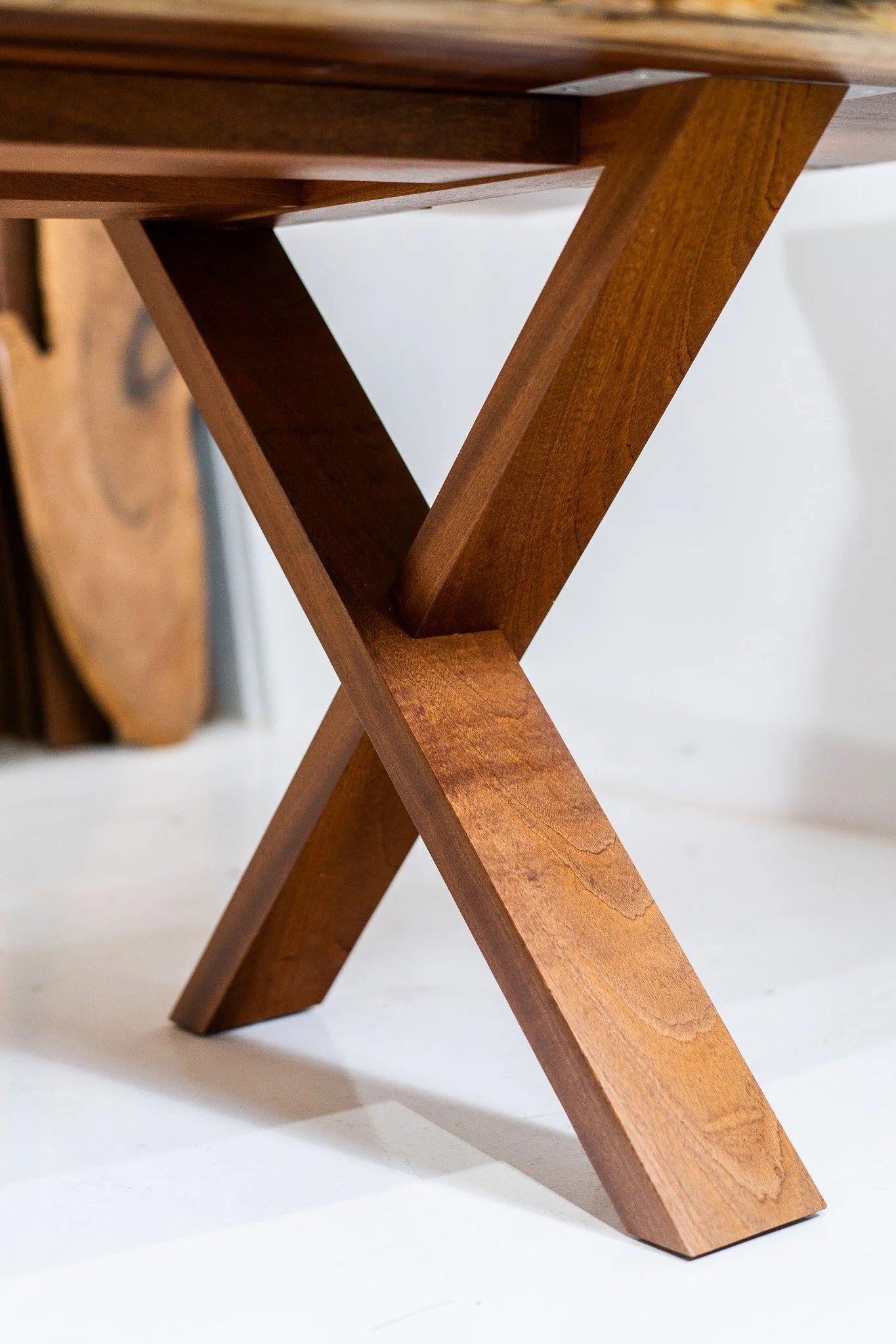 Close-up of a wooden table leg with a modern X-shaped design.