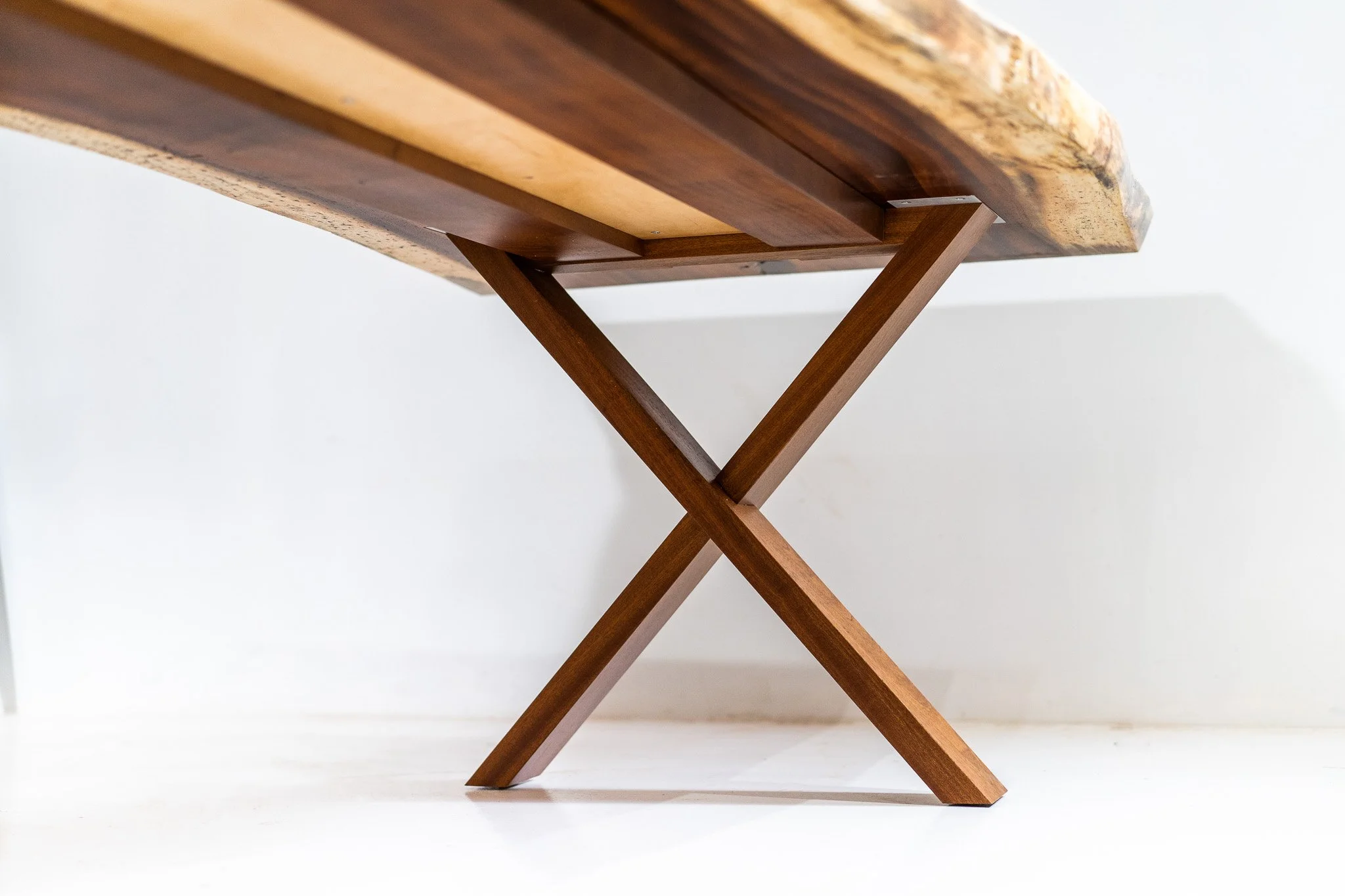 Close-up of a wooden table's underside showing its V-shaped leg design against a plain white background.