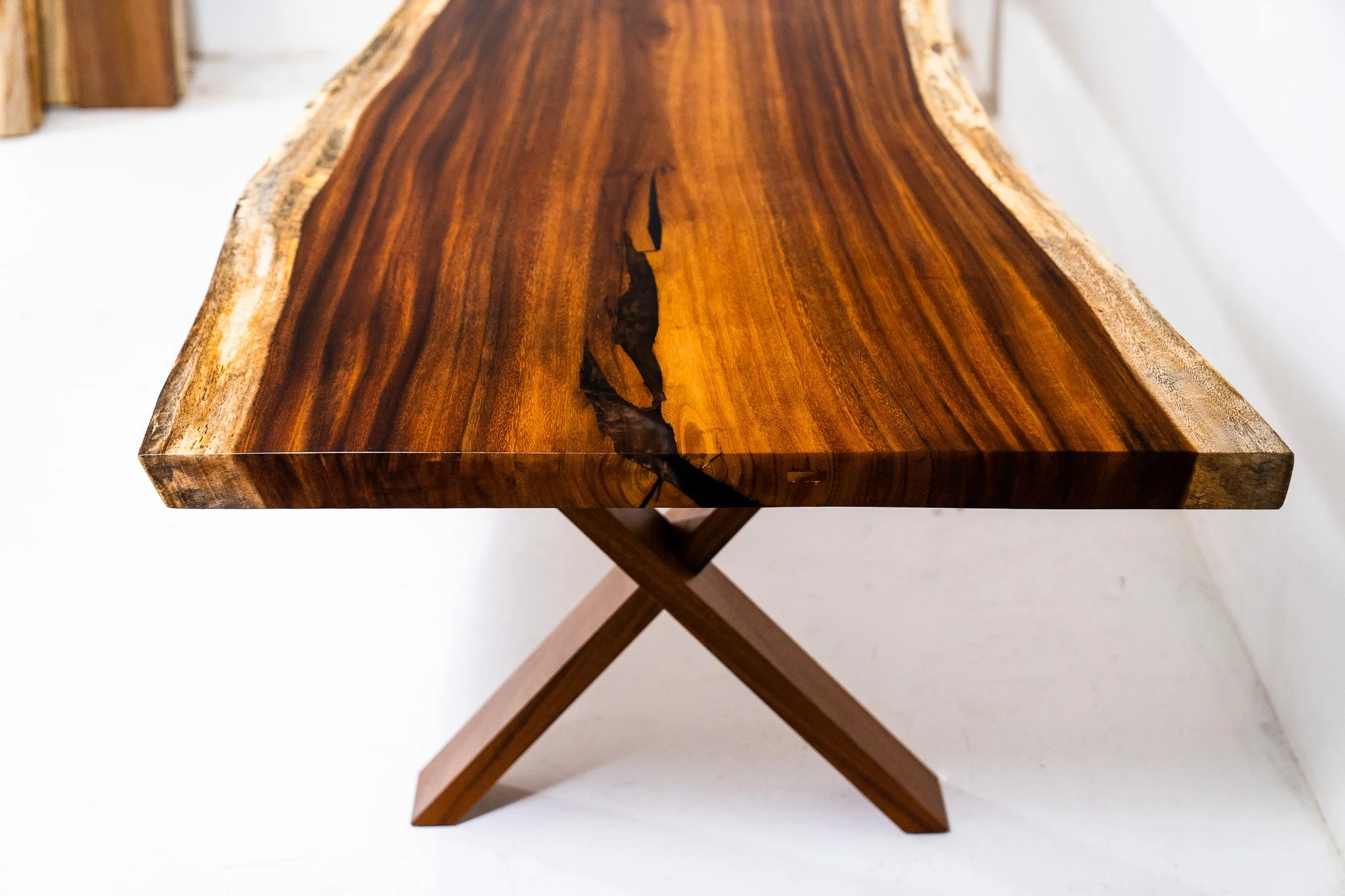 A wooden table with a natural, live edge finish and a prominent crack running down the center, supported by X-shaped legs.