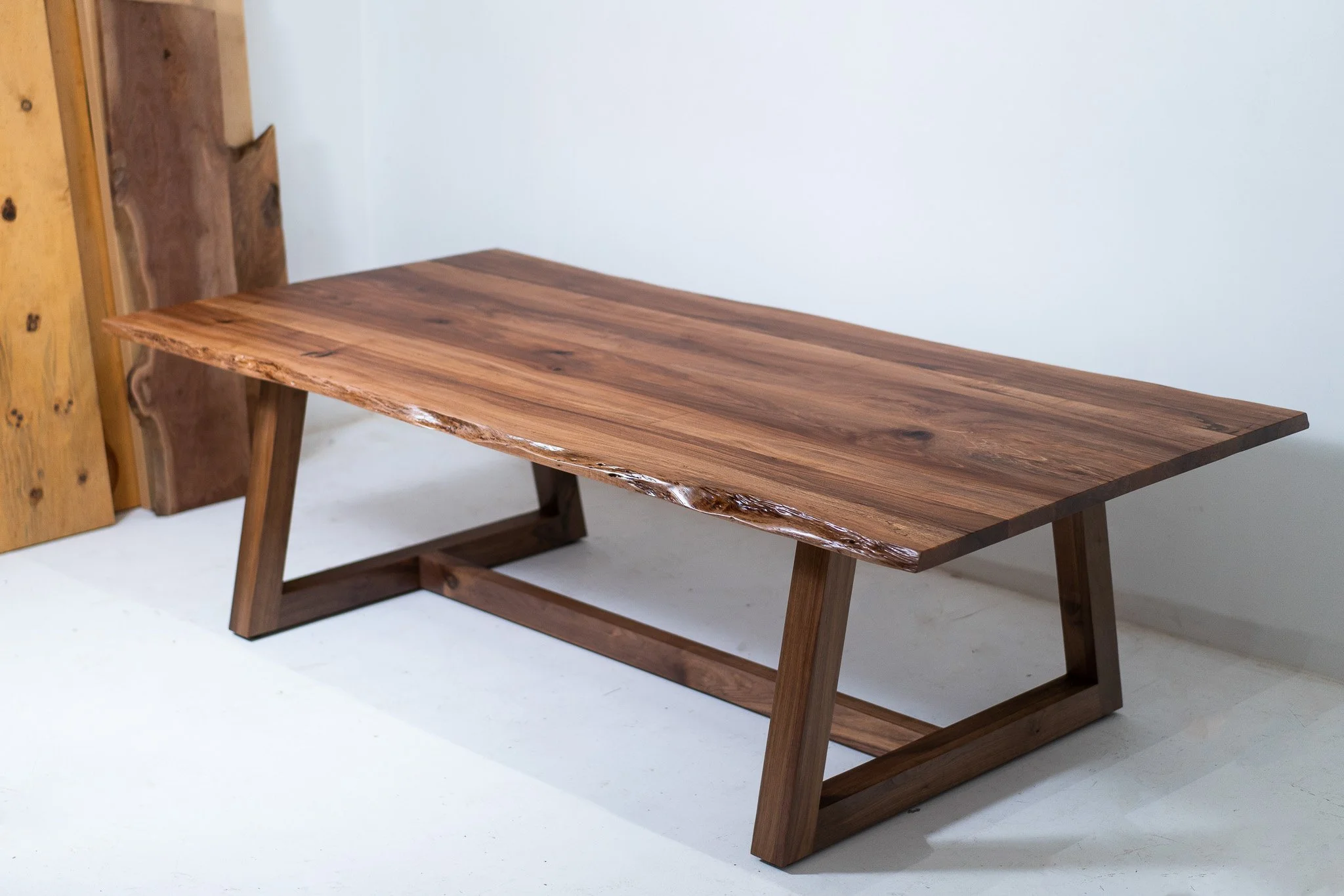 A modern wooden table with a natural edge and angled legs, placed against a plain white wall.