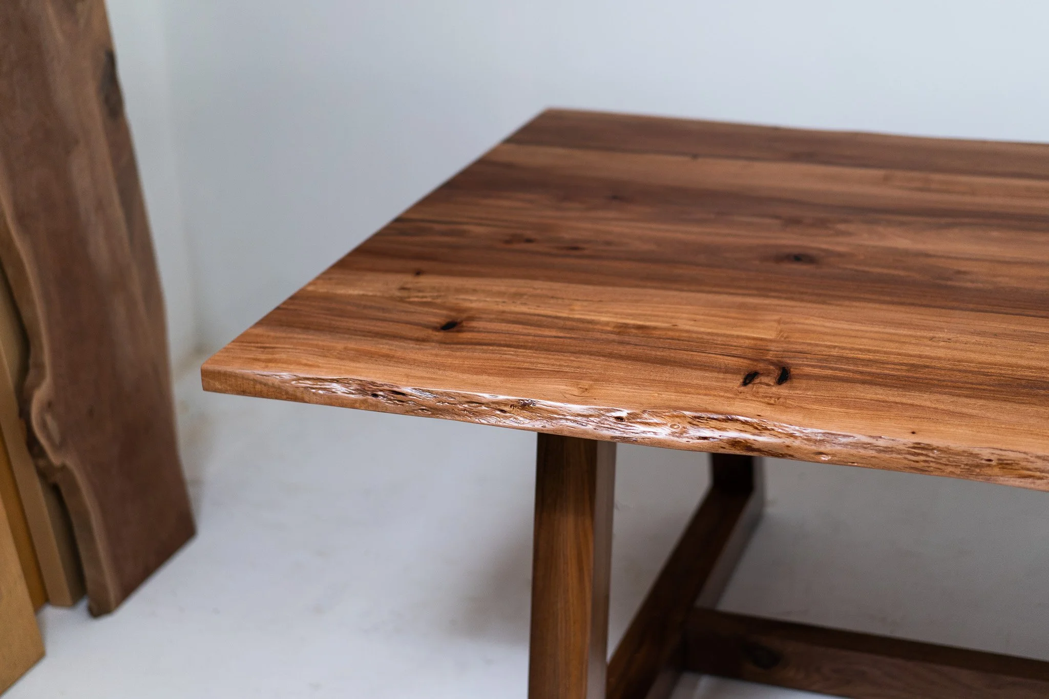Close-up of a wooden table with a natural edge, showing the wood grain and knots, against a plain light wall background.