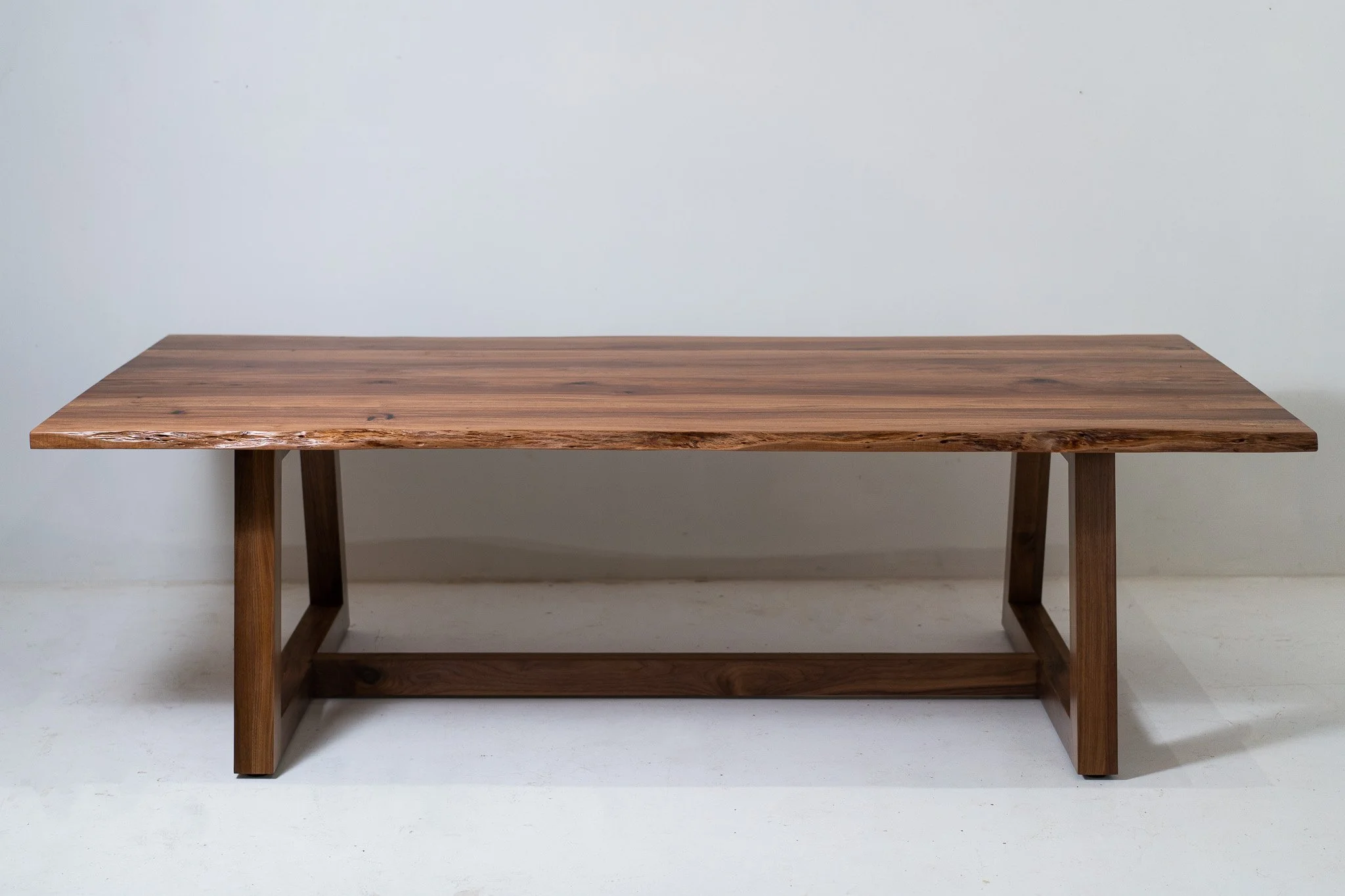 A wooden table with a rectangular top and sturdy legs against a plain white wall.