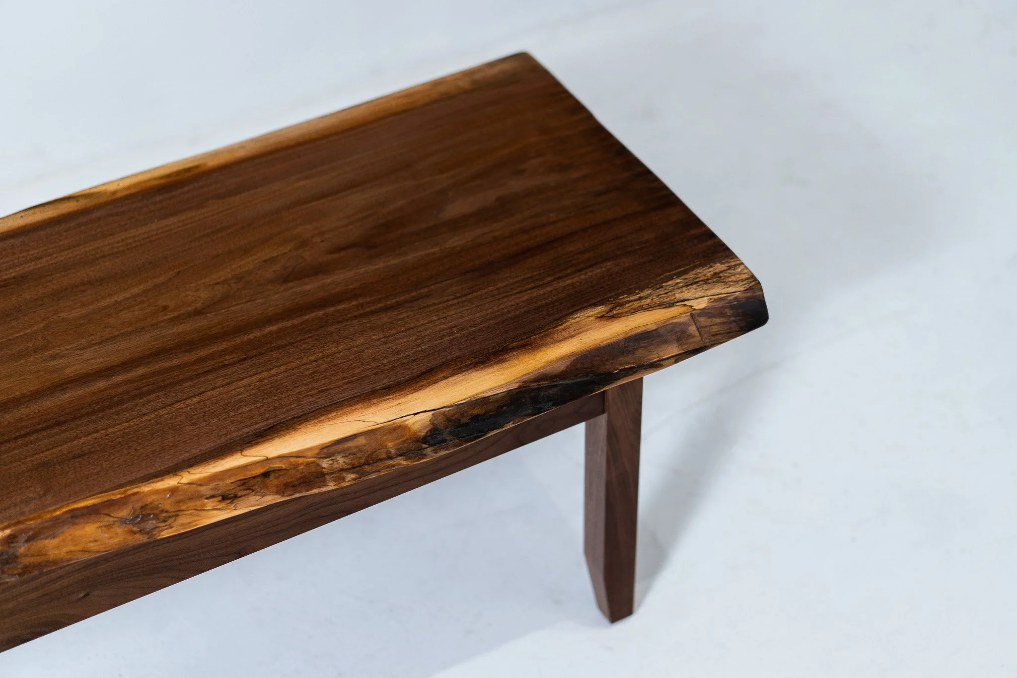 A wooden table with a natural edge and a dark finish, showing the grain and texture of the wood, against a plain white background.