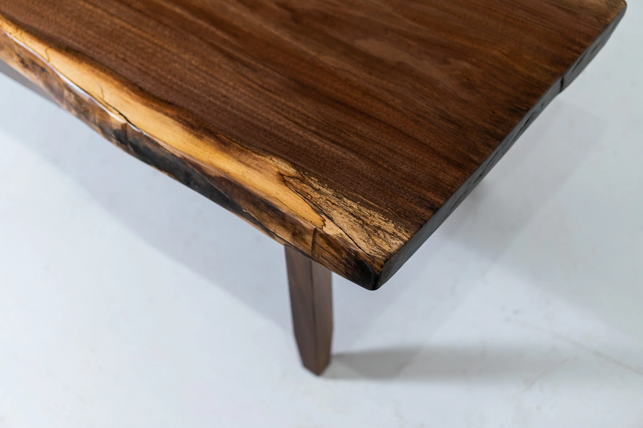Close-up of a wooden table corner showing a polished dark wood surface and a rounded edge with a natural wood grain pattern.