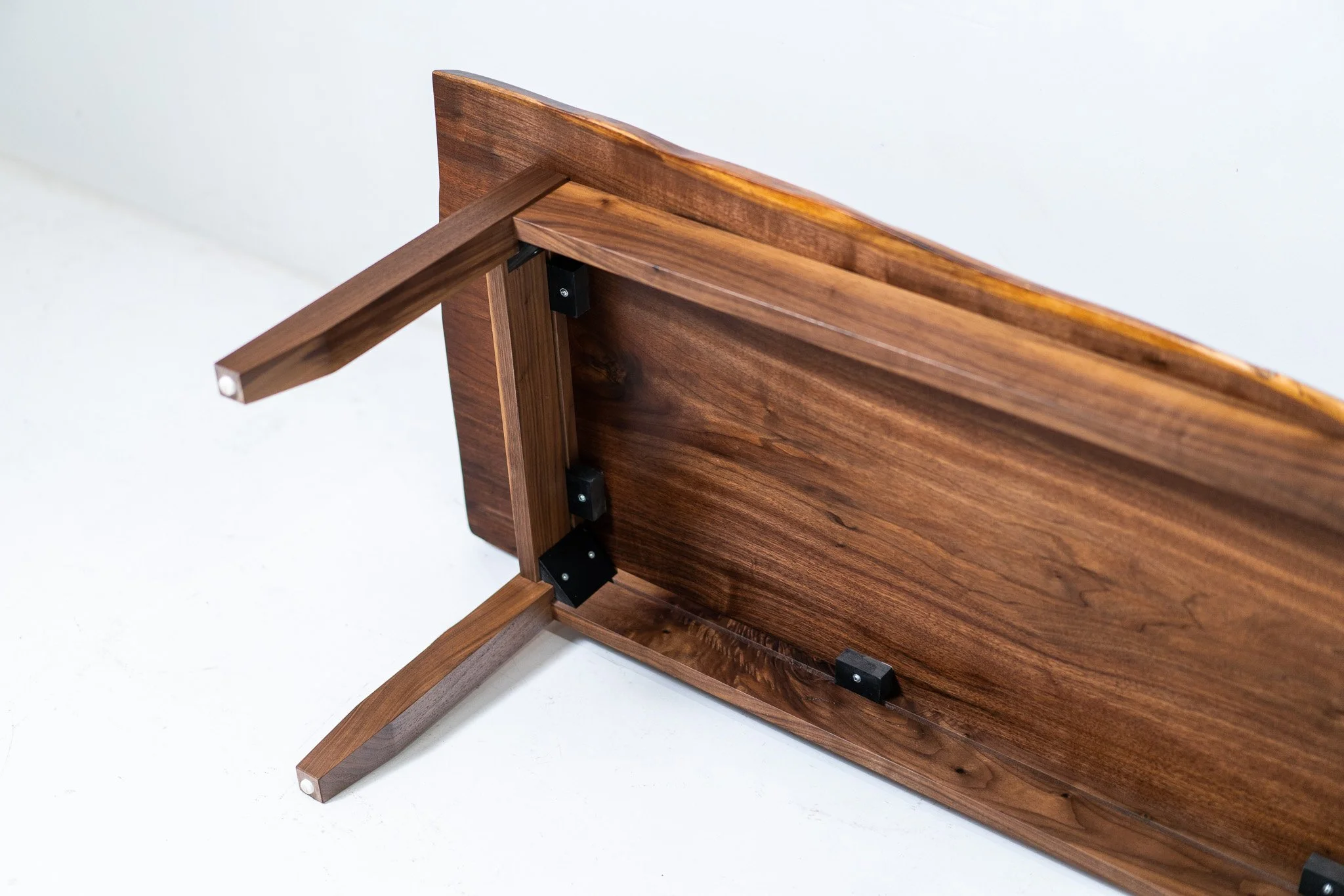 A wooden table turned upside down showing the underside with black hardware and joinery.