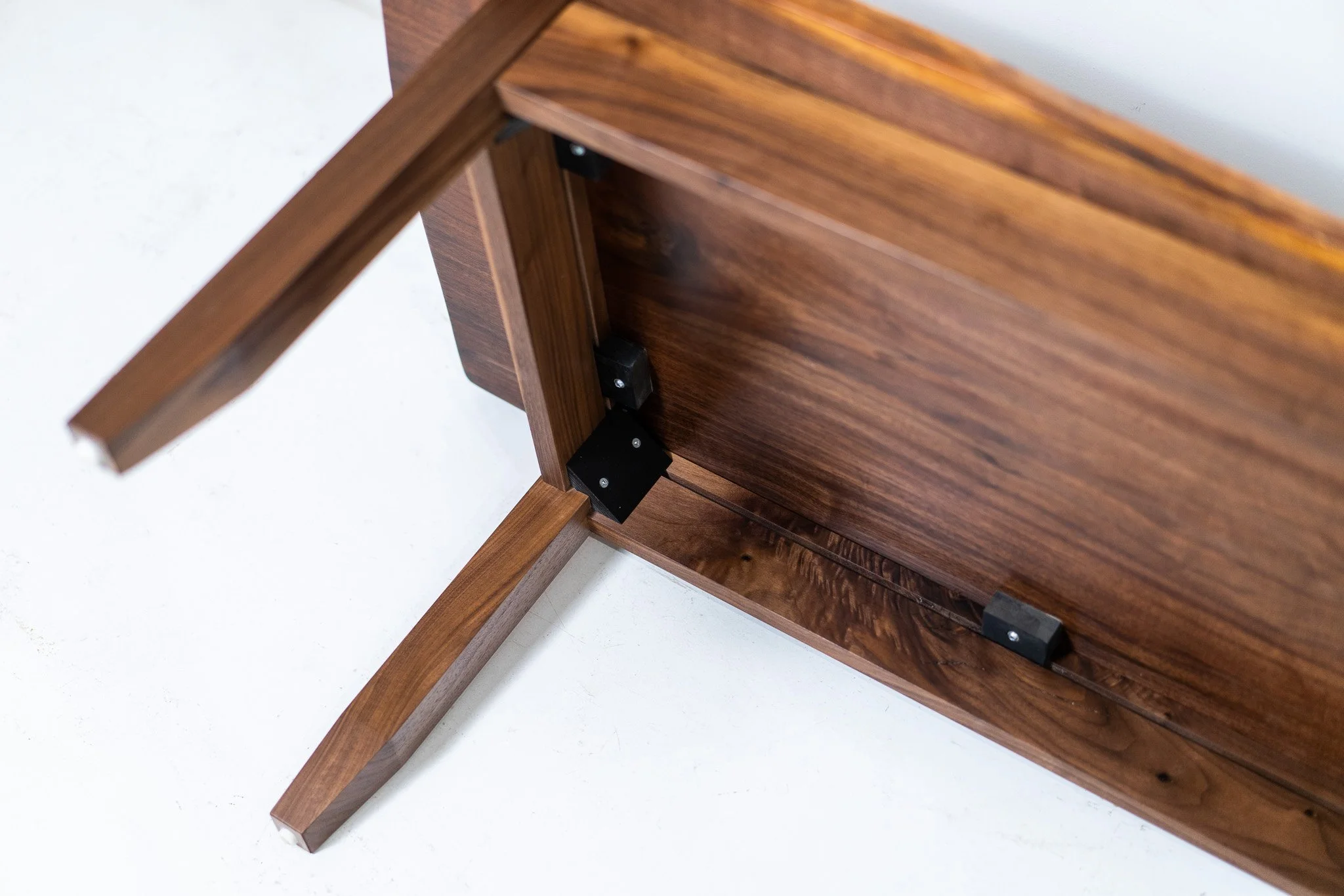Top view of a wooden table with an open underside showing black metal hinges and supports.