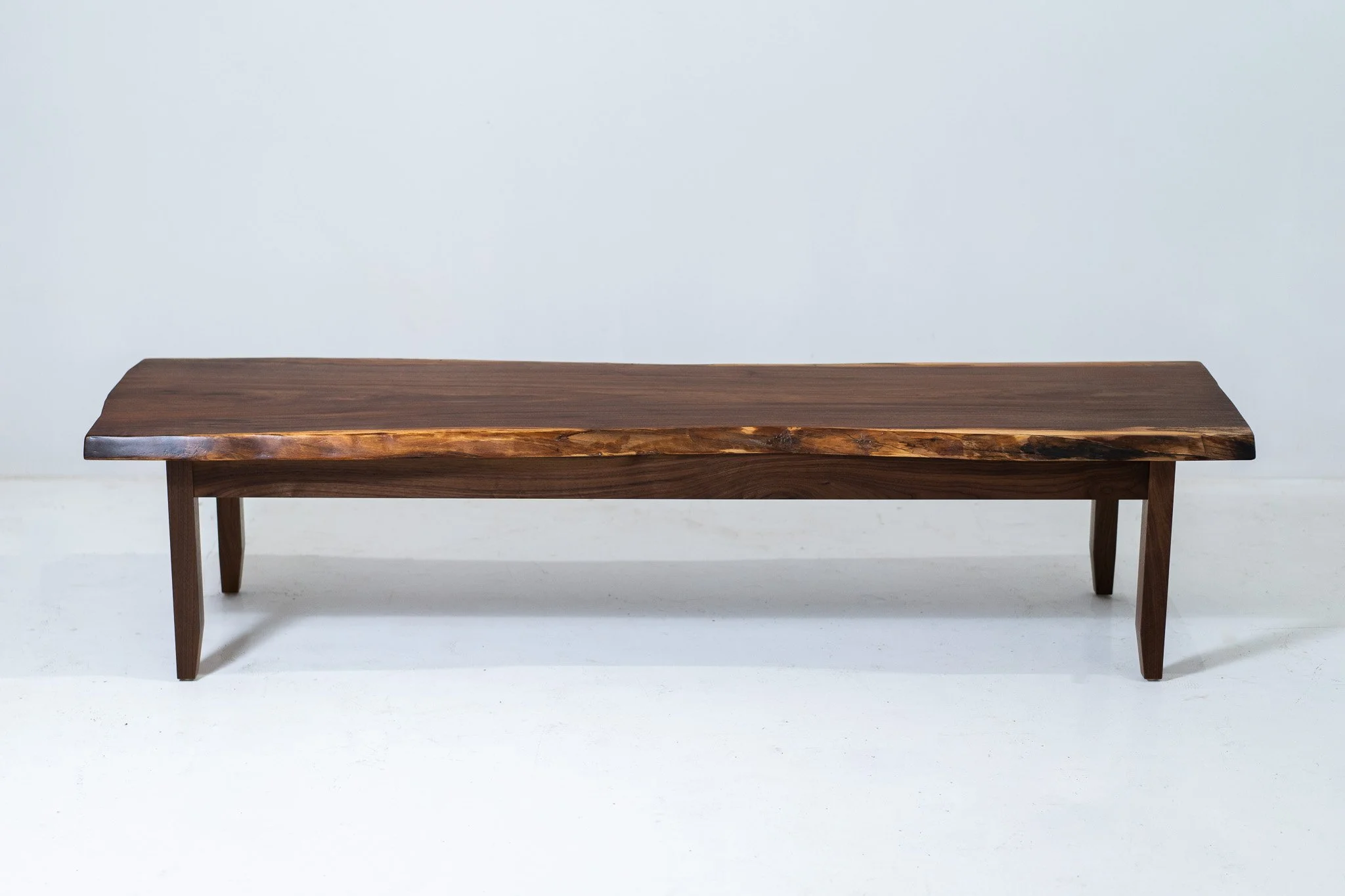 Minimalist wooden bench with a natural wood finish against a plain light background.