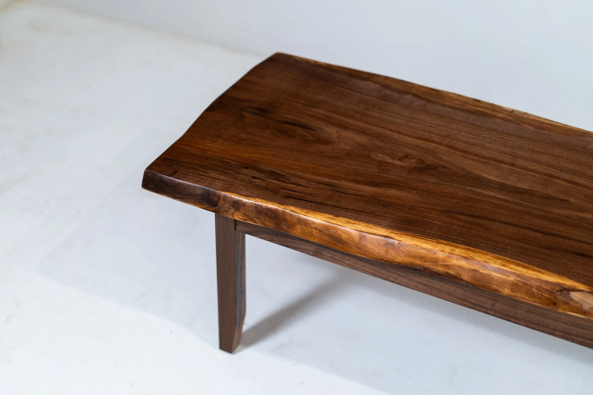 A close-up of a wooden bench with a smooth, polished surface and a natural wood grain, set against a light background.