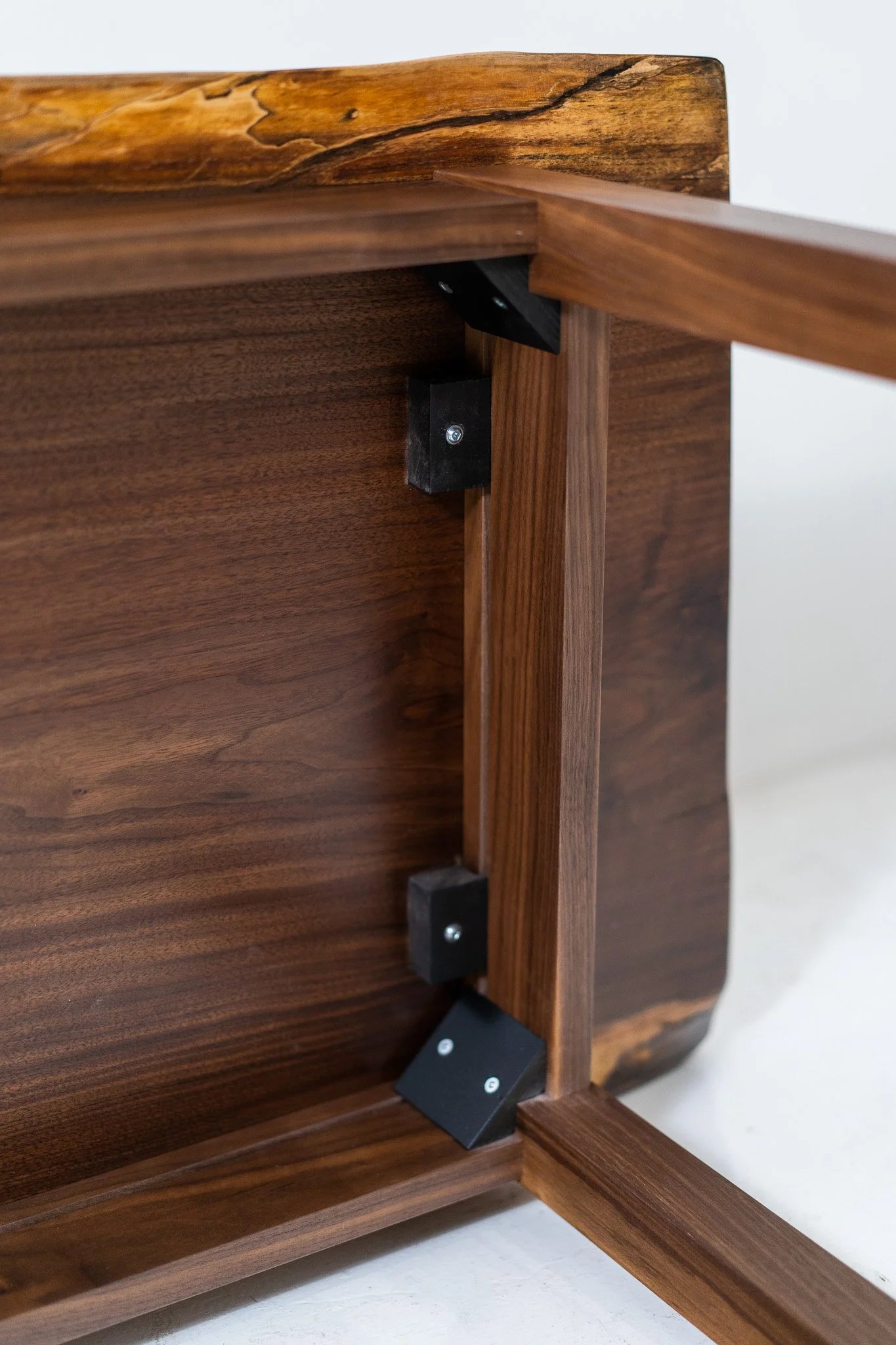 Close-up of the inside corner of a wooden piece of furniture showing metal brackets and screws securing the panels.