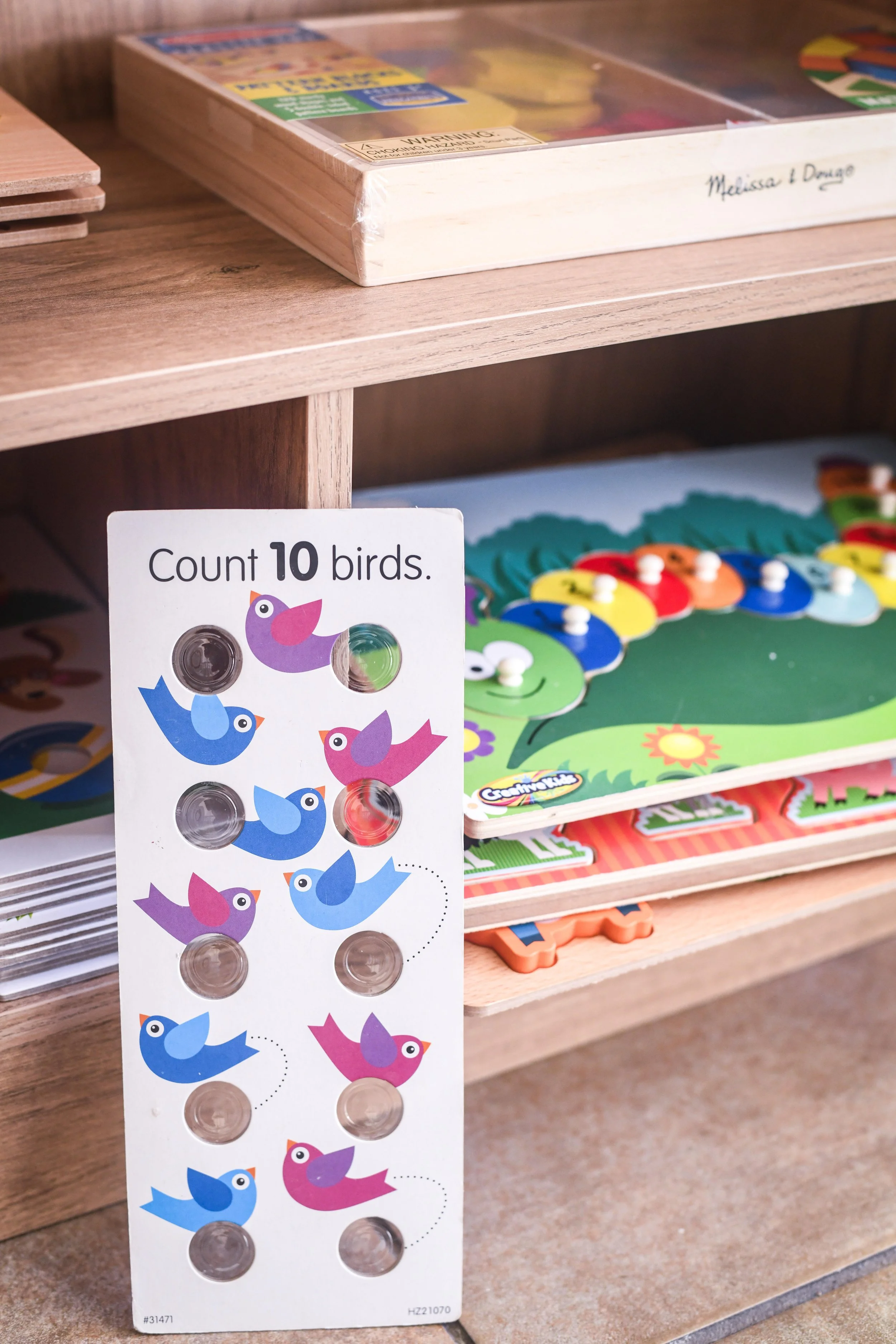 A colorful sticker sheet featuring various cartoon birds with speech bubbles, along with a partial view of children's educational board games on a wooden shelf.