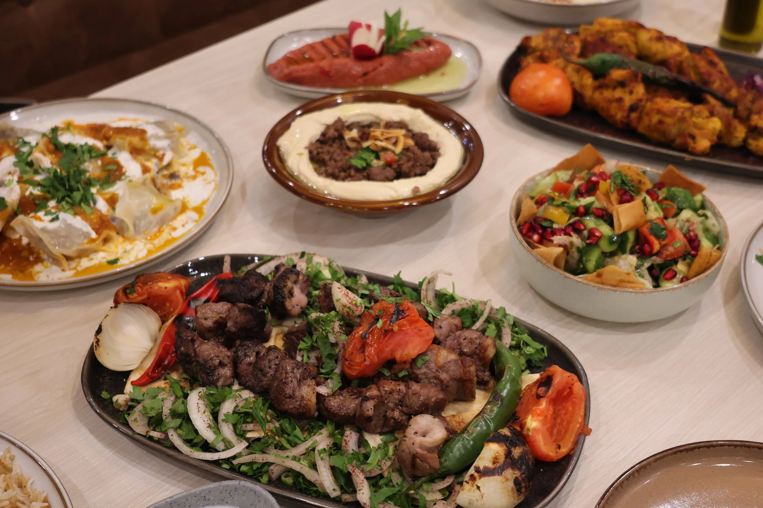 Assorted Middle Eastern dishes including kebabs, hummus, tabbouleh, grilled meats, and vegetables on a table.