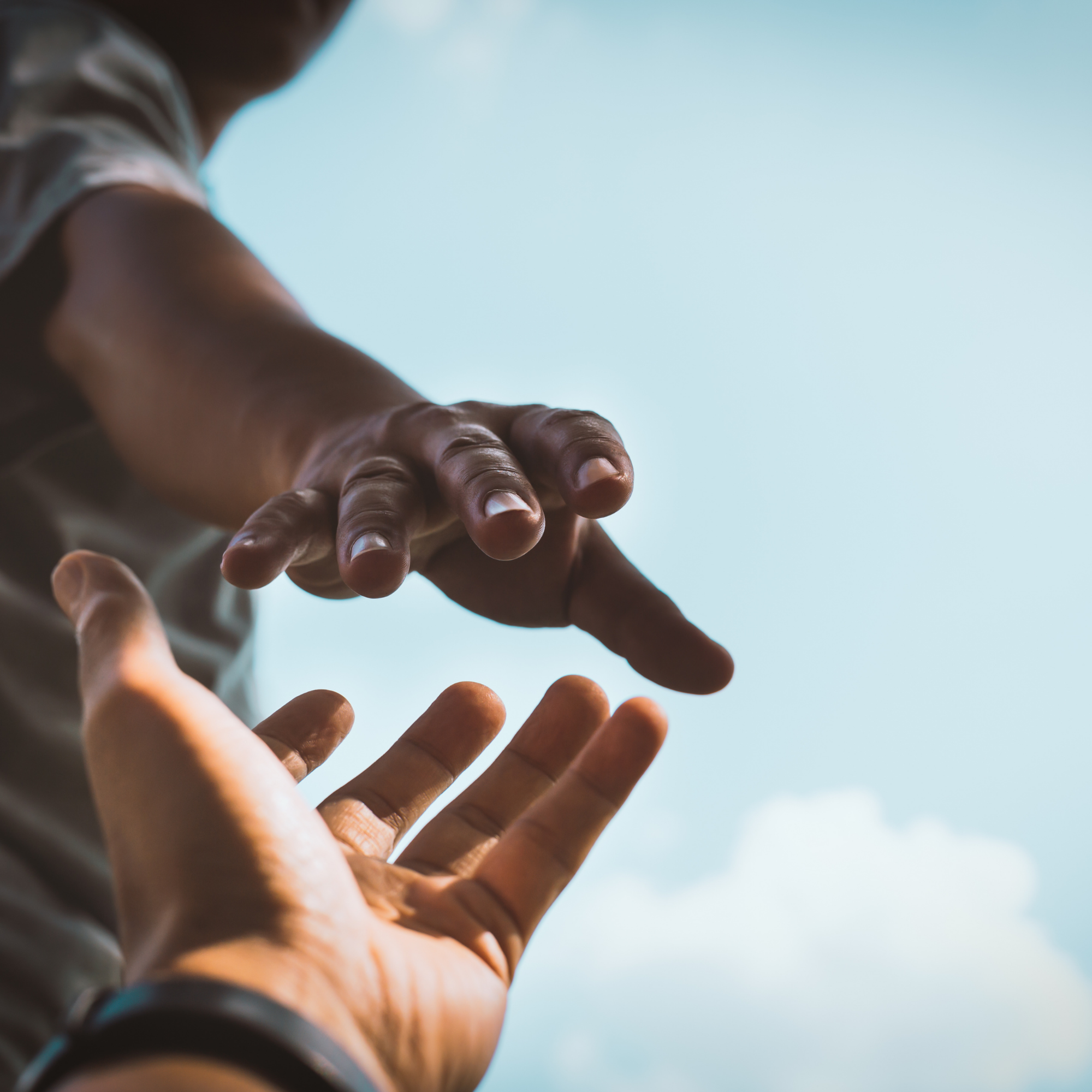 Two people reaching out their hands toward each other against a blue sky with clouds.