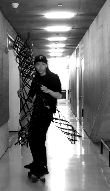 A person with long hair wearing a black hat and jacket riding a skateboard in a corridor.