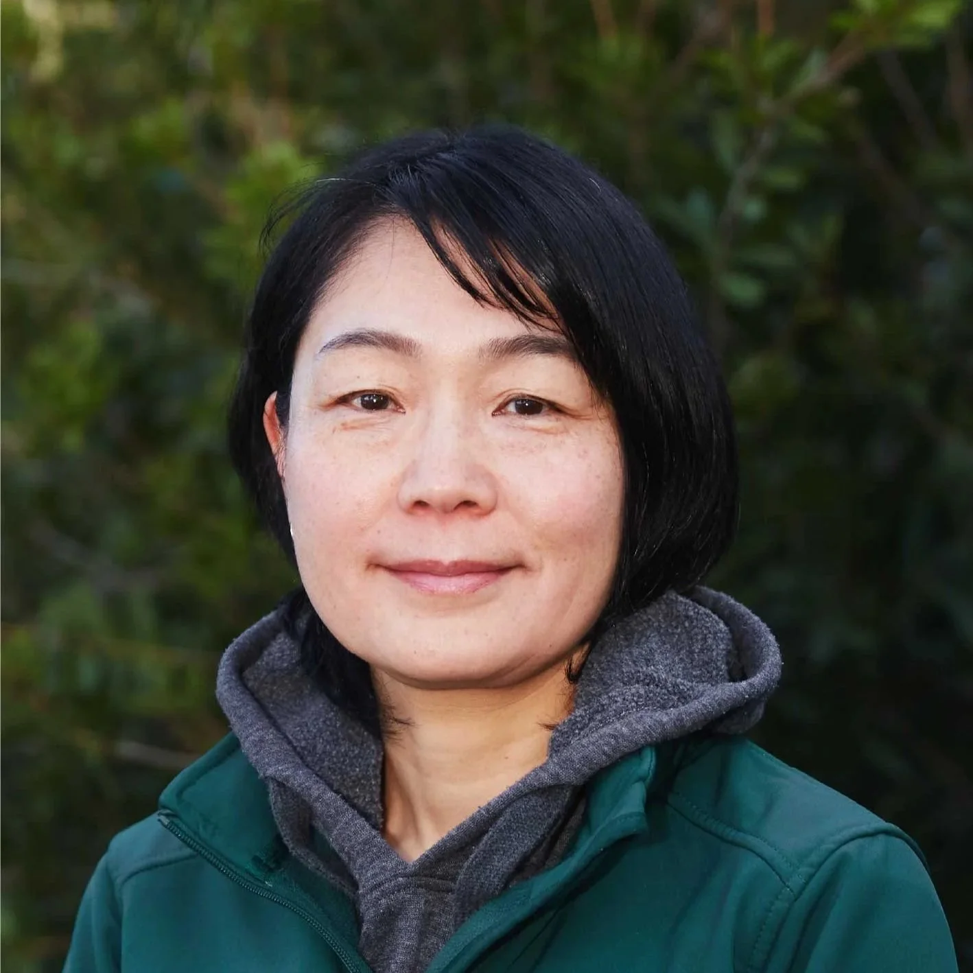 A smiling woman with shoulder-length black hair standing in front of a brick wall.