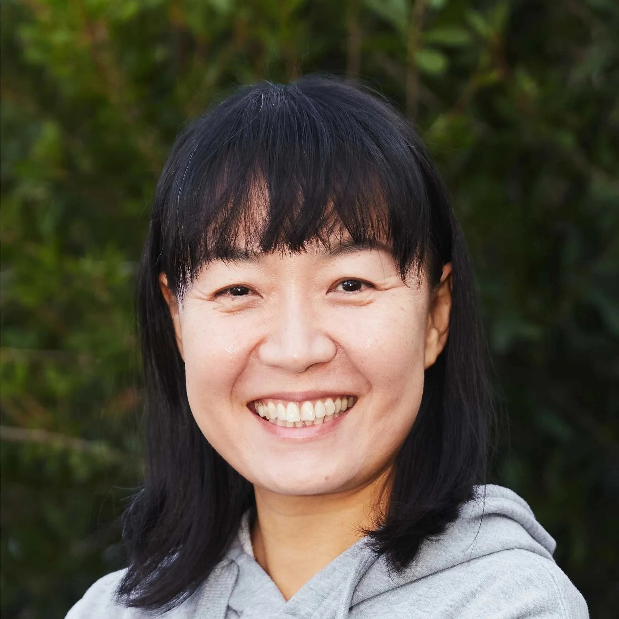 A smiling woman with shoulder-length black hair standing in front of a brick wall.