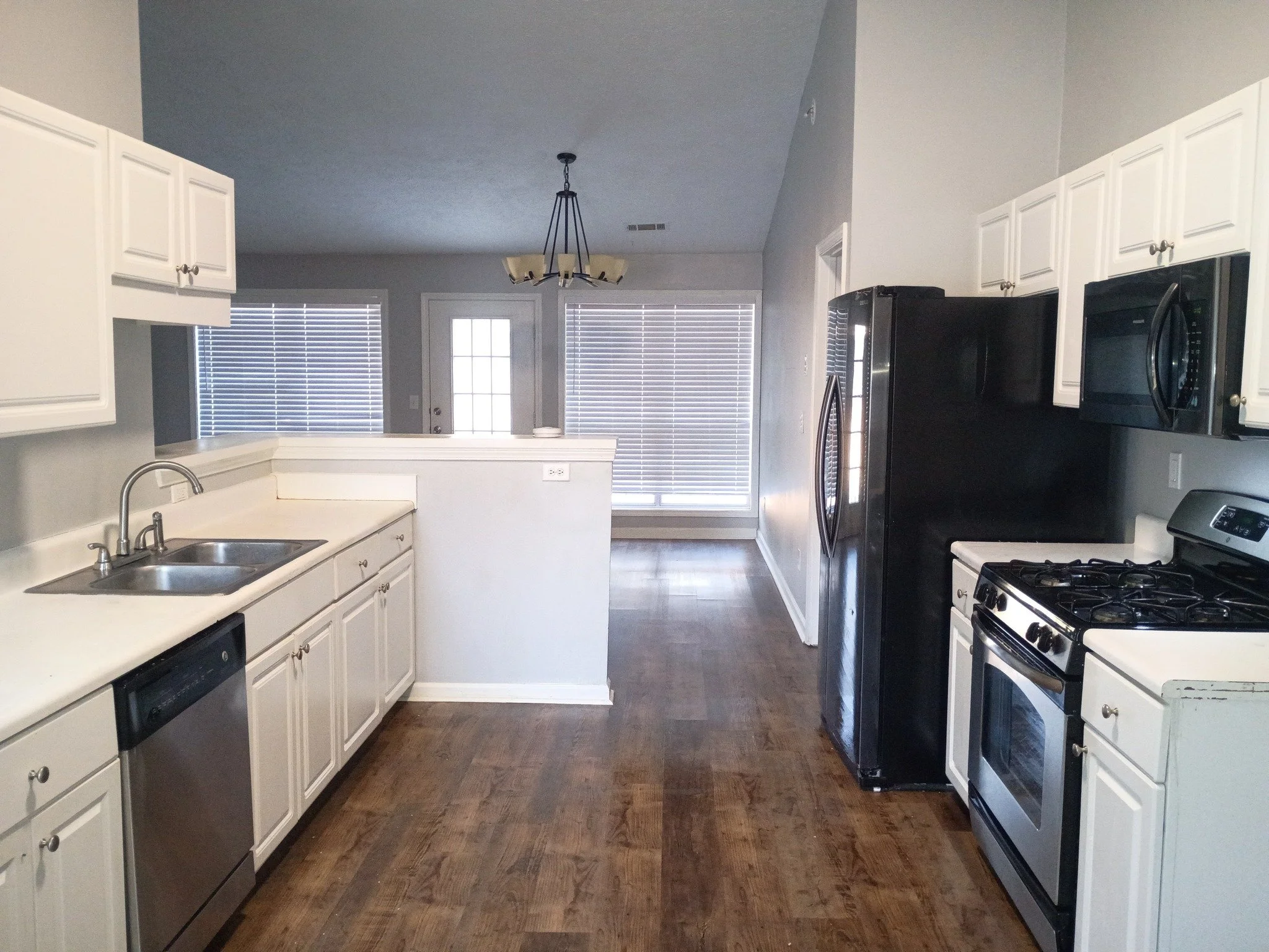 Kitchen with white cabinets, wood flooring, black refrigerator, and stainless steel appliances, view toward back door with large windows and blinds. Kitchen cleaning in dekalb county georgia 