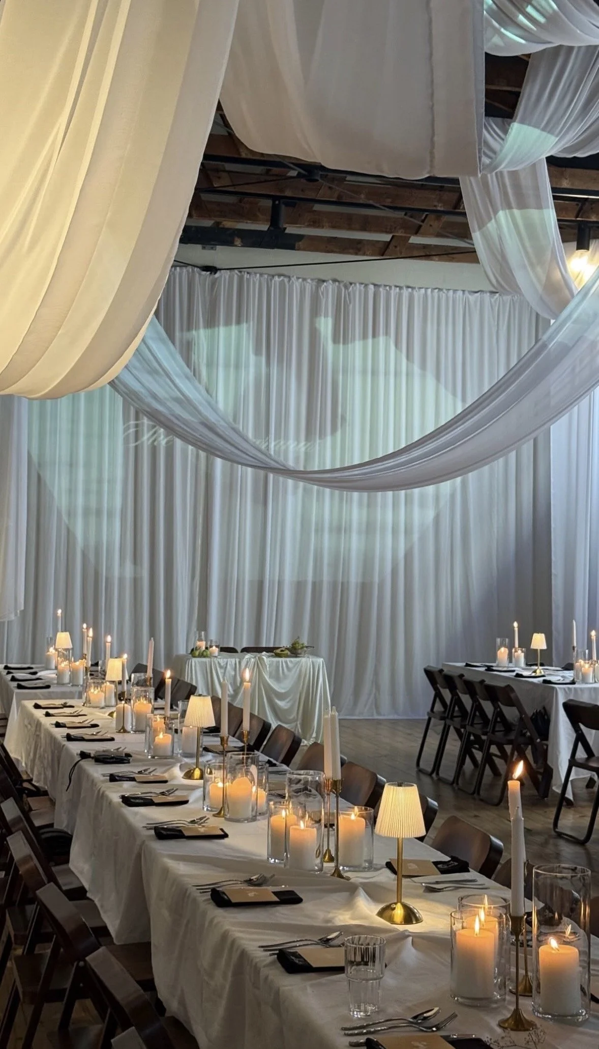 Decorated venue with draped white fabric and candles on table, set for a formal event or dinner.