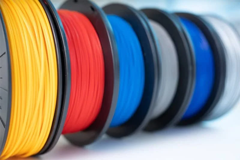 Spools of filament in yellow, red, blue, black, and gray for 3D printing.