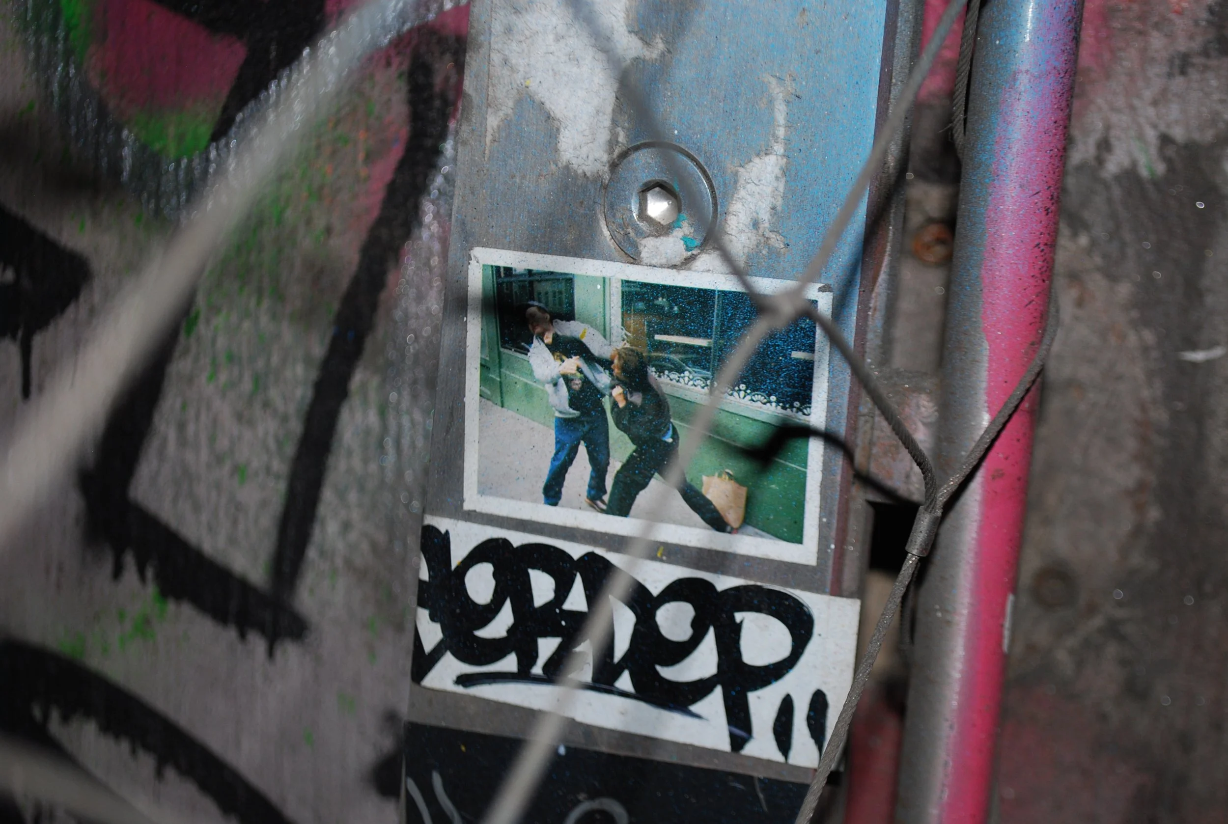Graffiti-covered wall with a sticker of two people fighting in an indoor setting.