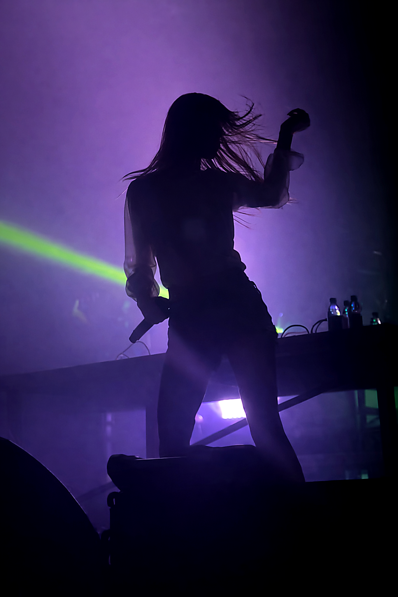 Silhouette of a female DJ performing on stage with purple and green lighting and a digital table with water bottles.
