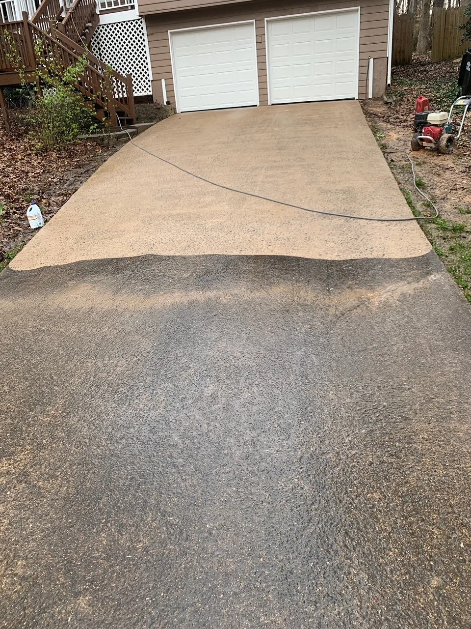 A driveway being coated with fresh asphalt, with a transition between old black asphalt and new tan-colored asphalt leading to a garage.