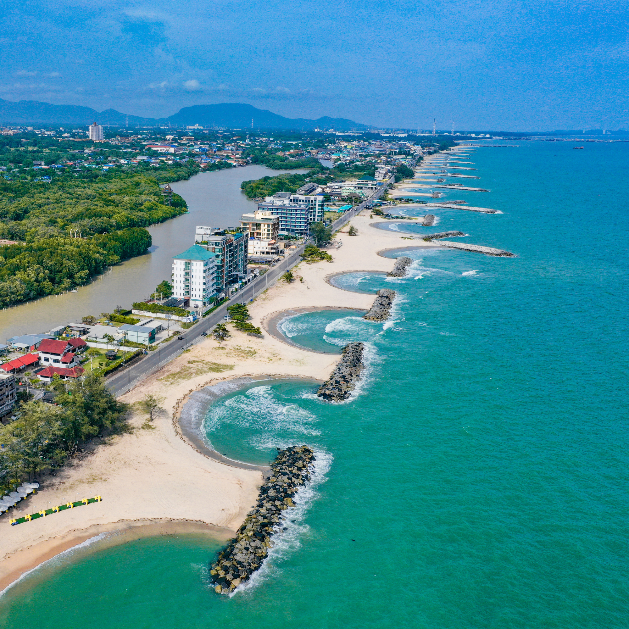 Aerial view of a coastal city with a beach, ocean, buildings, and mountains in the distance.
