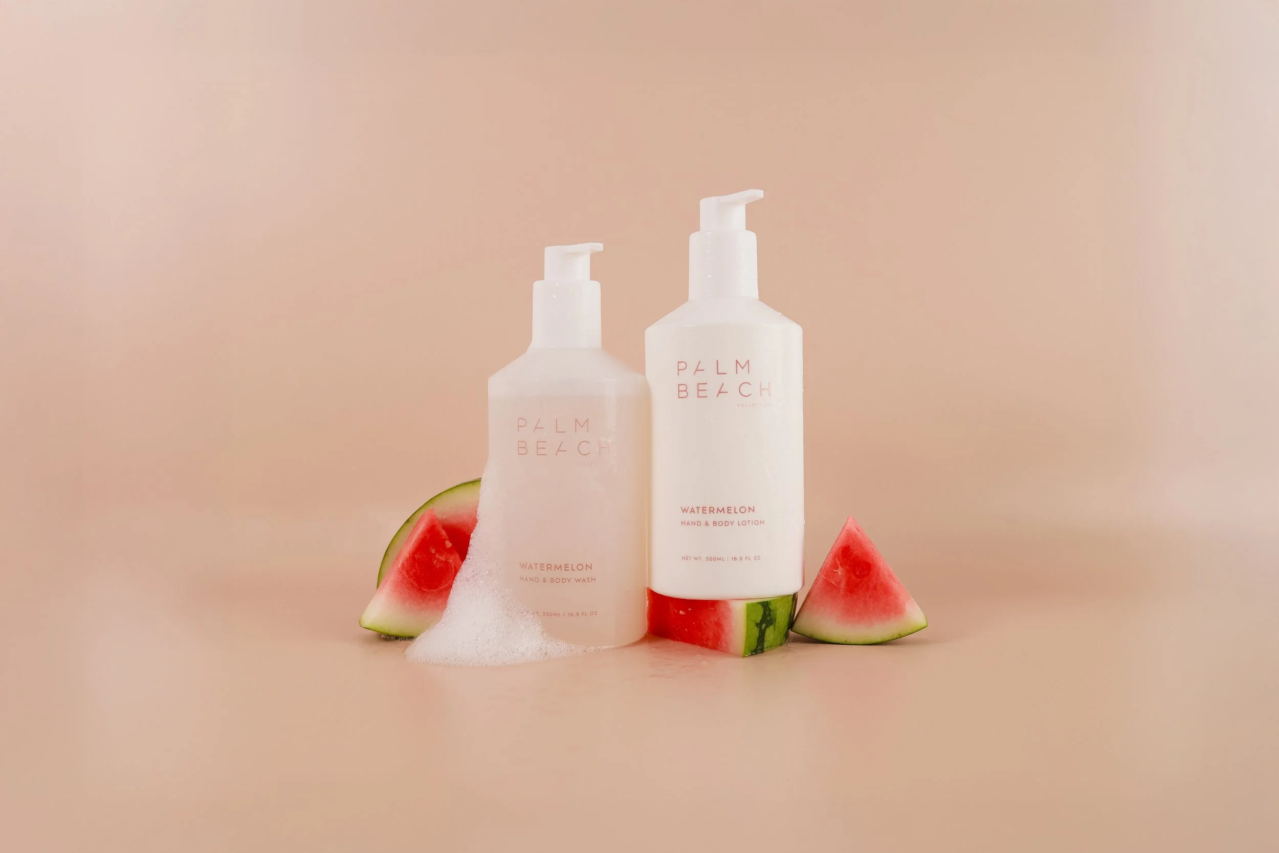 Two white bottles of Palm Beach watermelon scented hand and body lotion and wash surrounded by slices of watermelon on a beige background.
