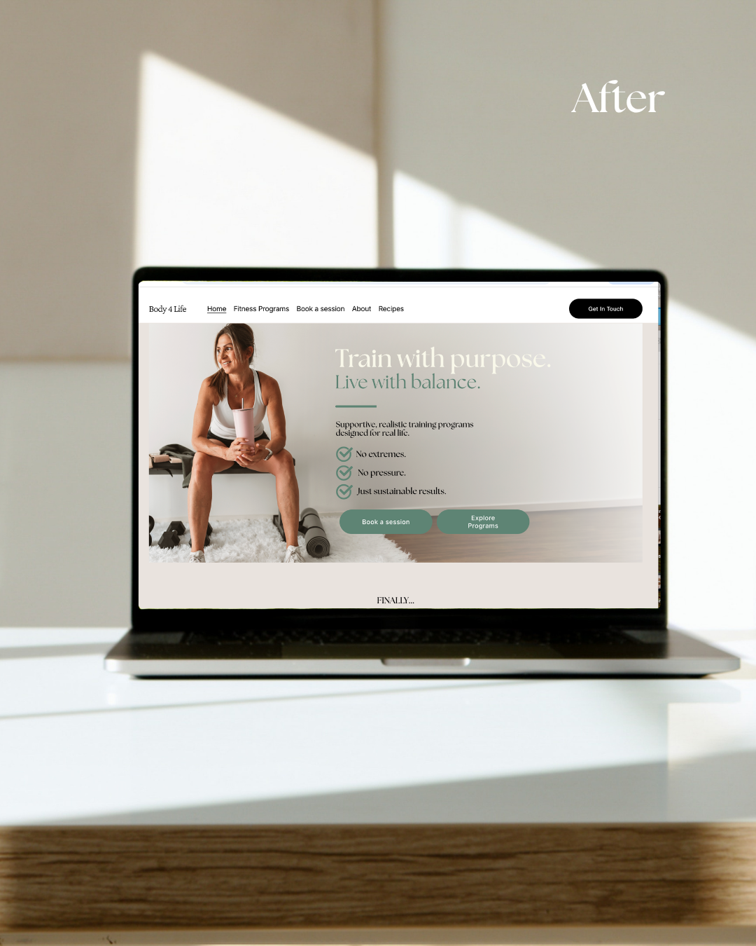 Laptop displaying a fitness website with a woman in workout attire sitting with a water bottle, on a white surface with sunlight streaming in.