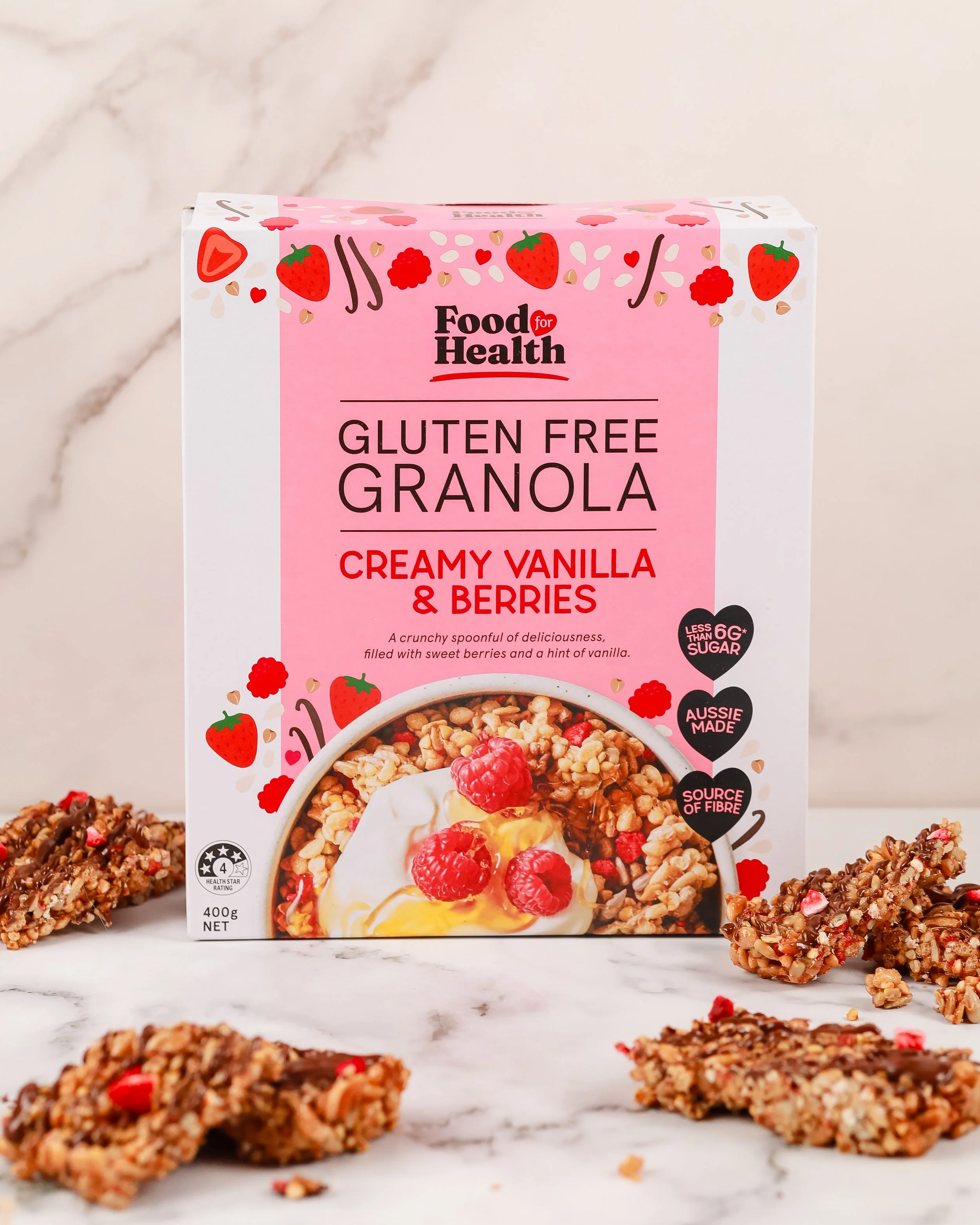 A box of gluten-free granola with strawberries and berries, surrounded by granola bars on a marble surface.